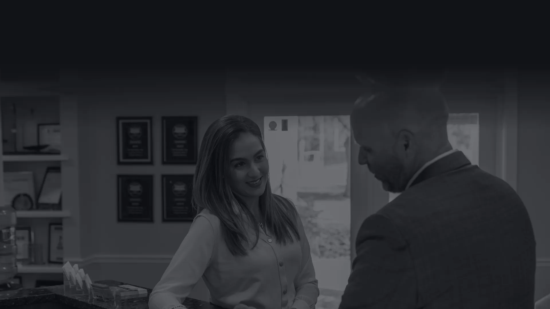 Receptionist handing a card to a man in a suit at a welcoming office front desk.
