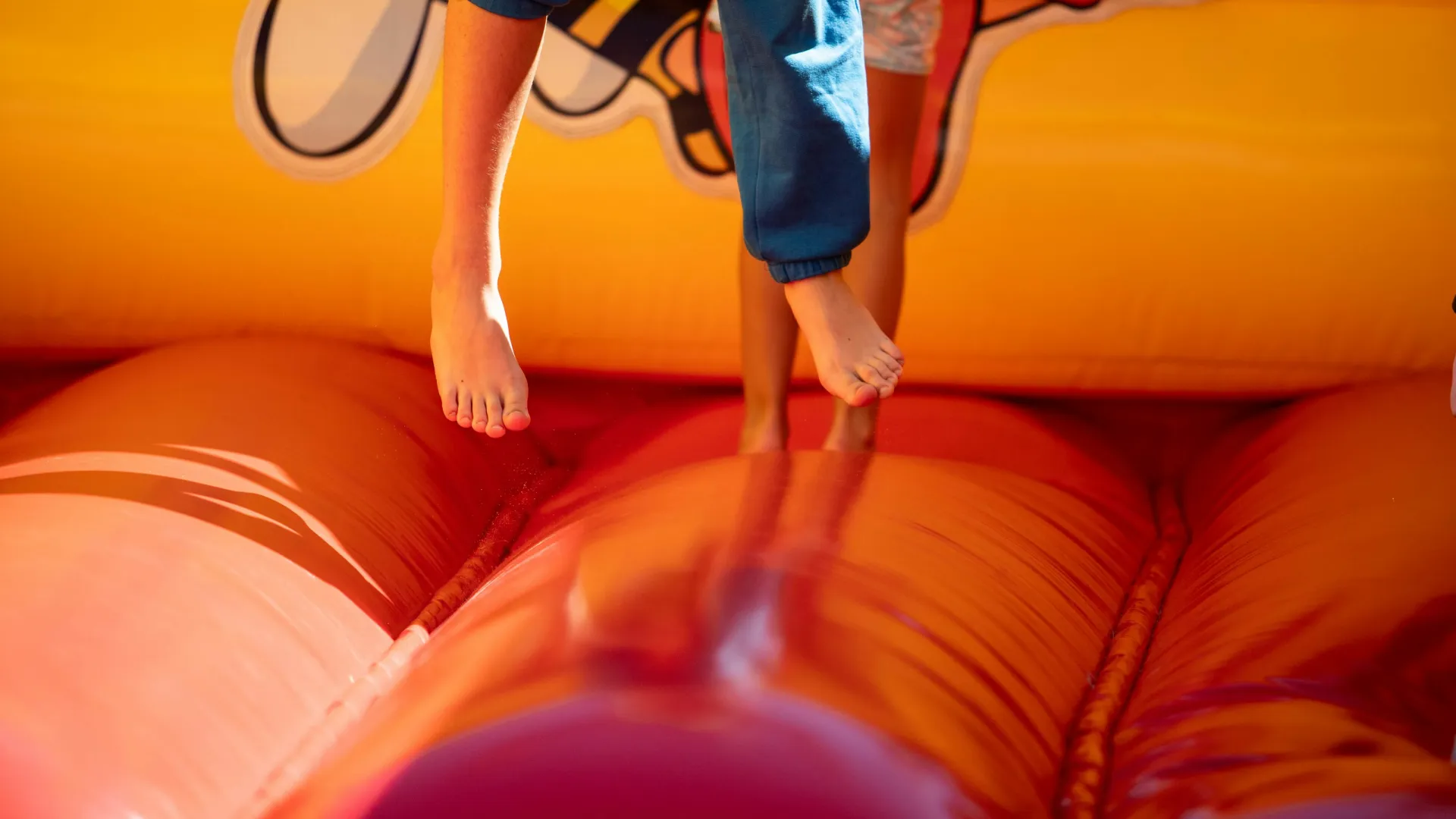 Children's bare feet bouncing on a vibrant red inflatable bounce house under bright light.