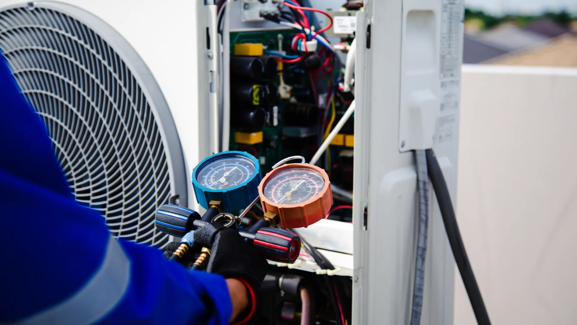 Technician using gauges to check and service an outdoor air conditioning unit on a rooftop.