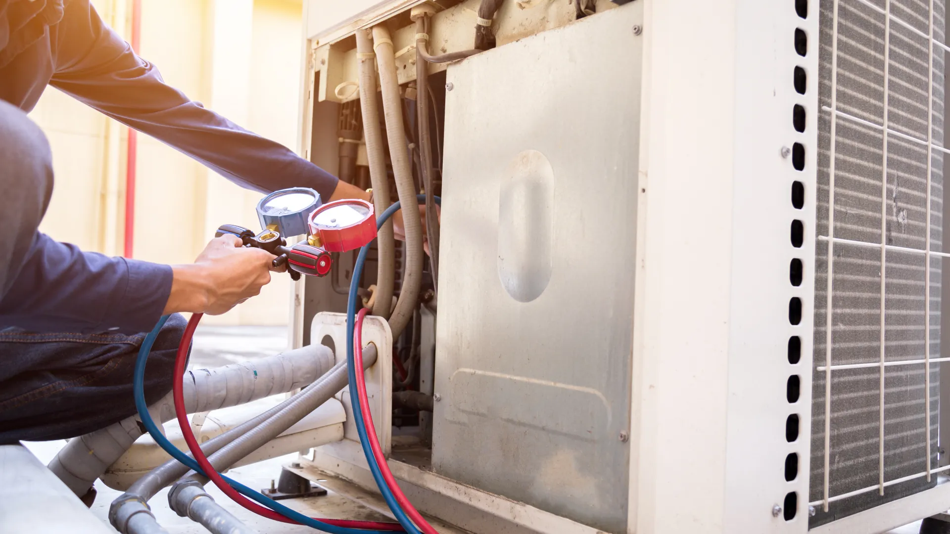 Technician servicing an air conditioning unit using gauges and hoses to check performance and repairs.