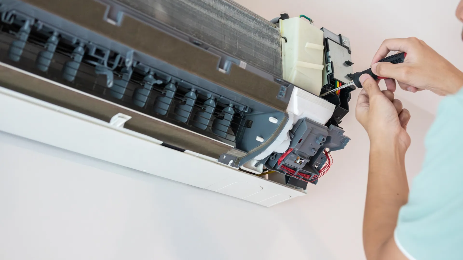 Technician repairing the internal components of a wall-mounted air conditioning unit with a screwdriver.