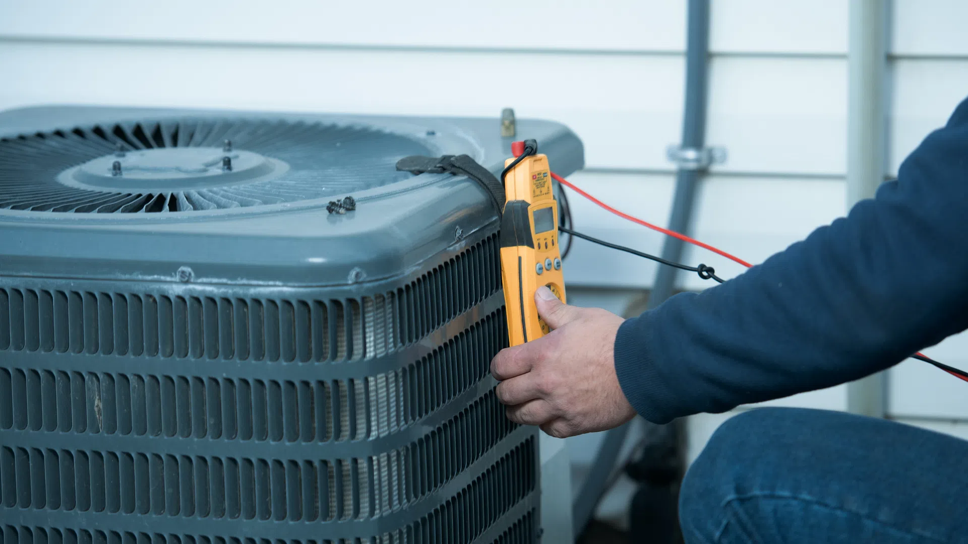 Technician using a multimeter to test an outdoor air conditioning unit against house siding.
