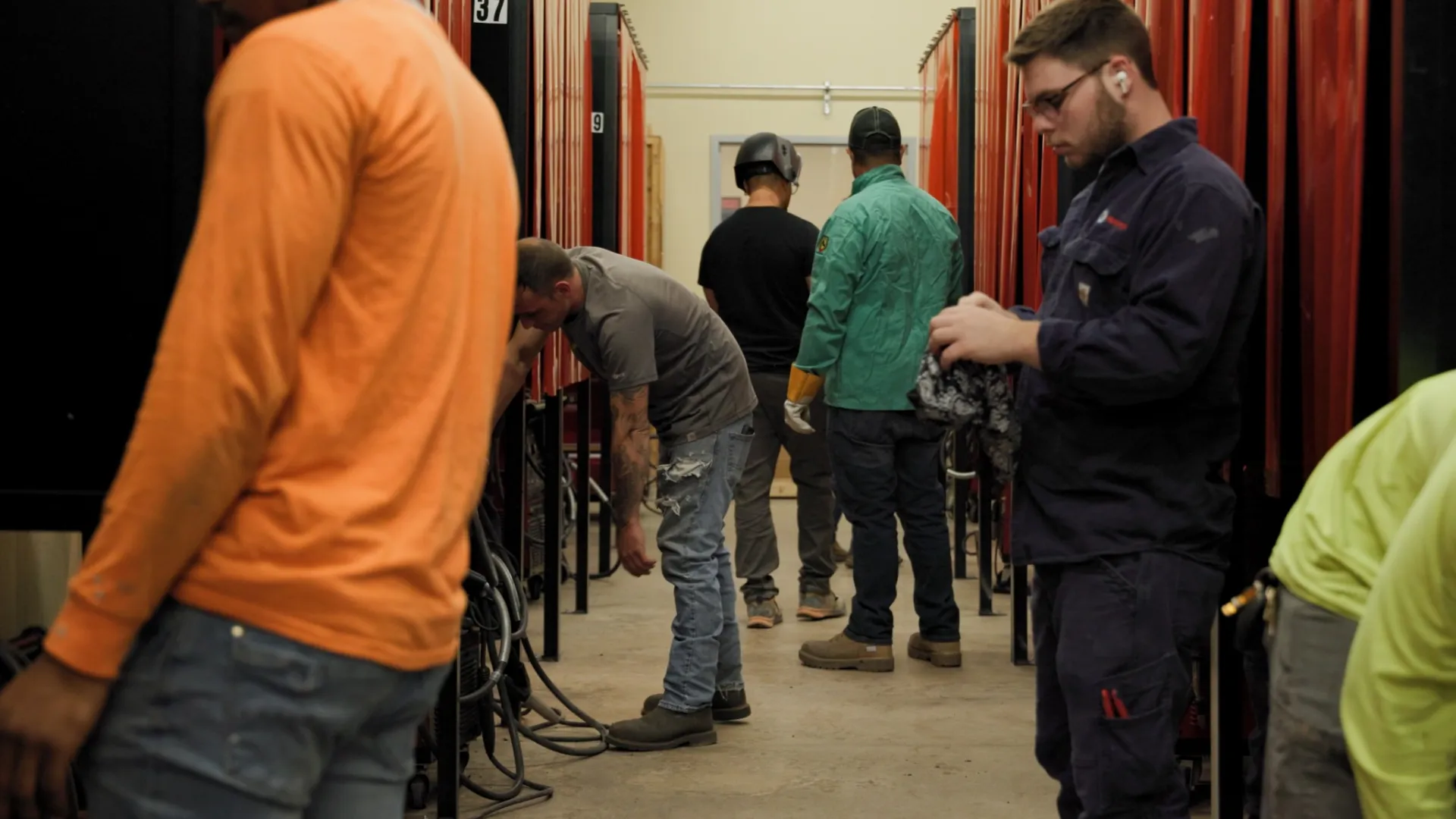 Workers in protective gear operating welding stations in a workshop with numbered curtains dividing each area