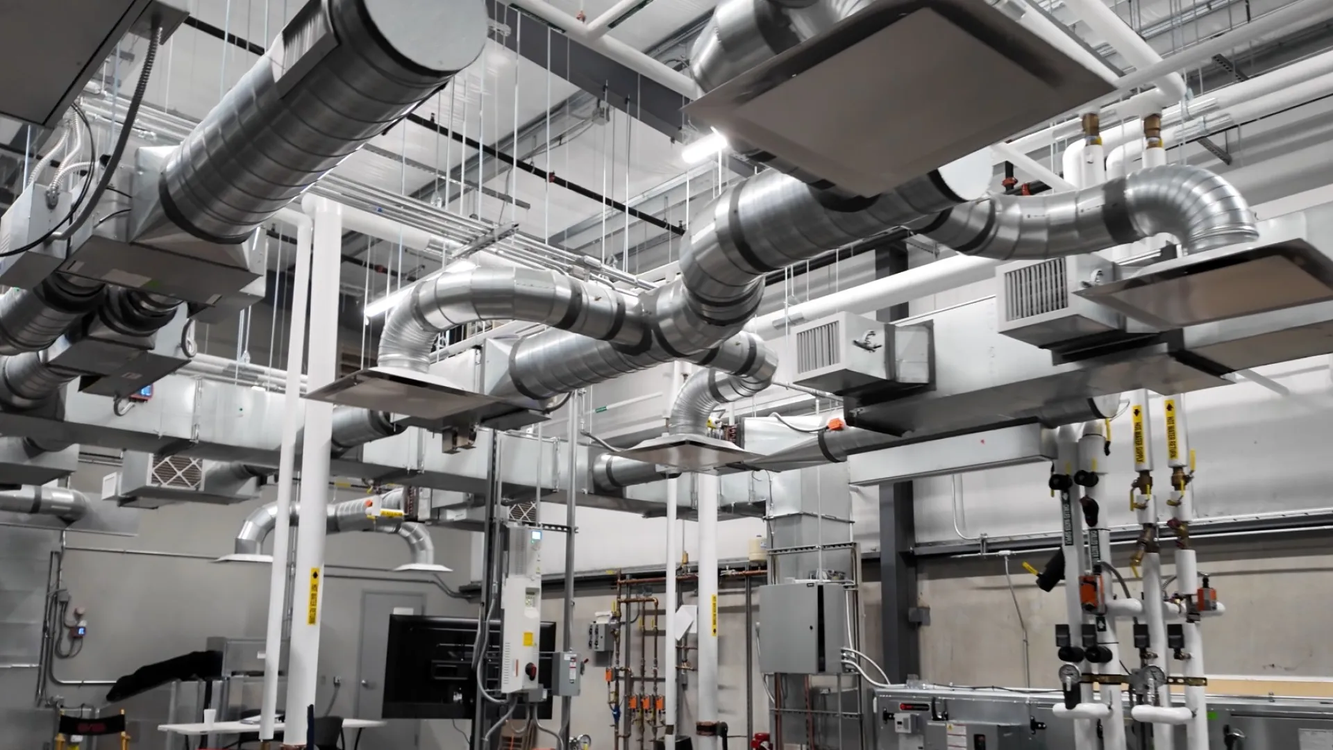 Industrial HVAC system with large ductwork, pipes, and equipment in a spacious facility interior.