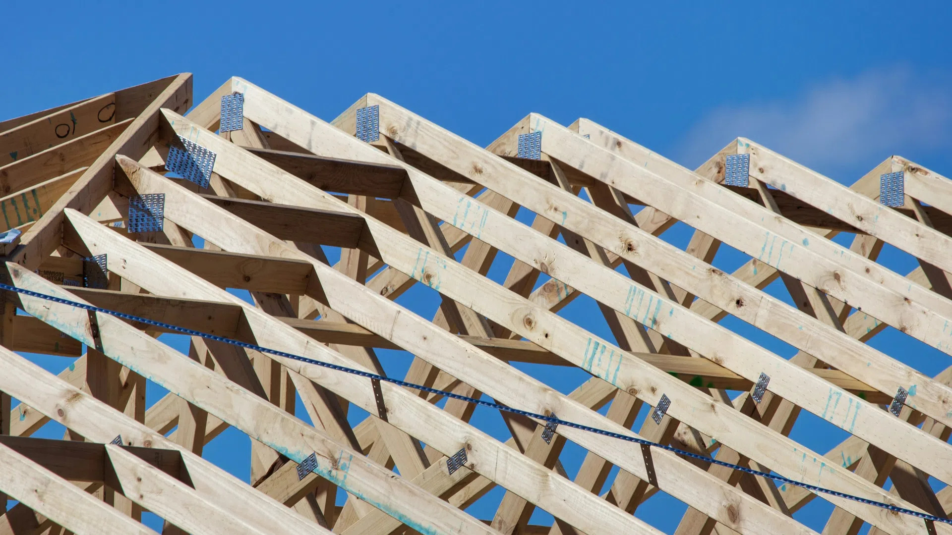 Wooden roof trusses under construction against a clear blue sky during daytime.