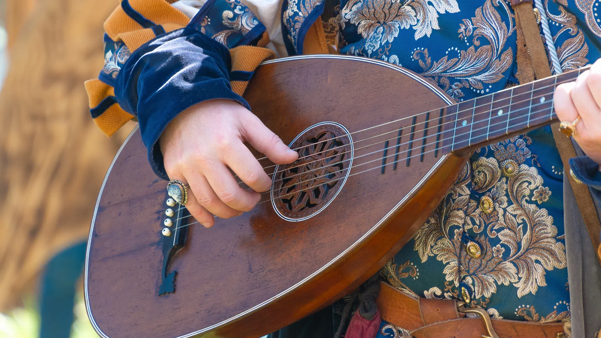 Close-up of hands playing a vintage lute with ornate blue and gold medieval costume details.