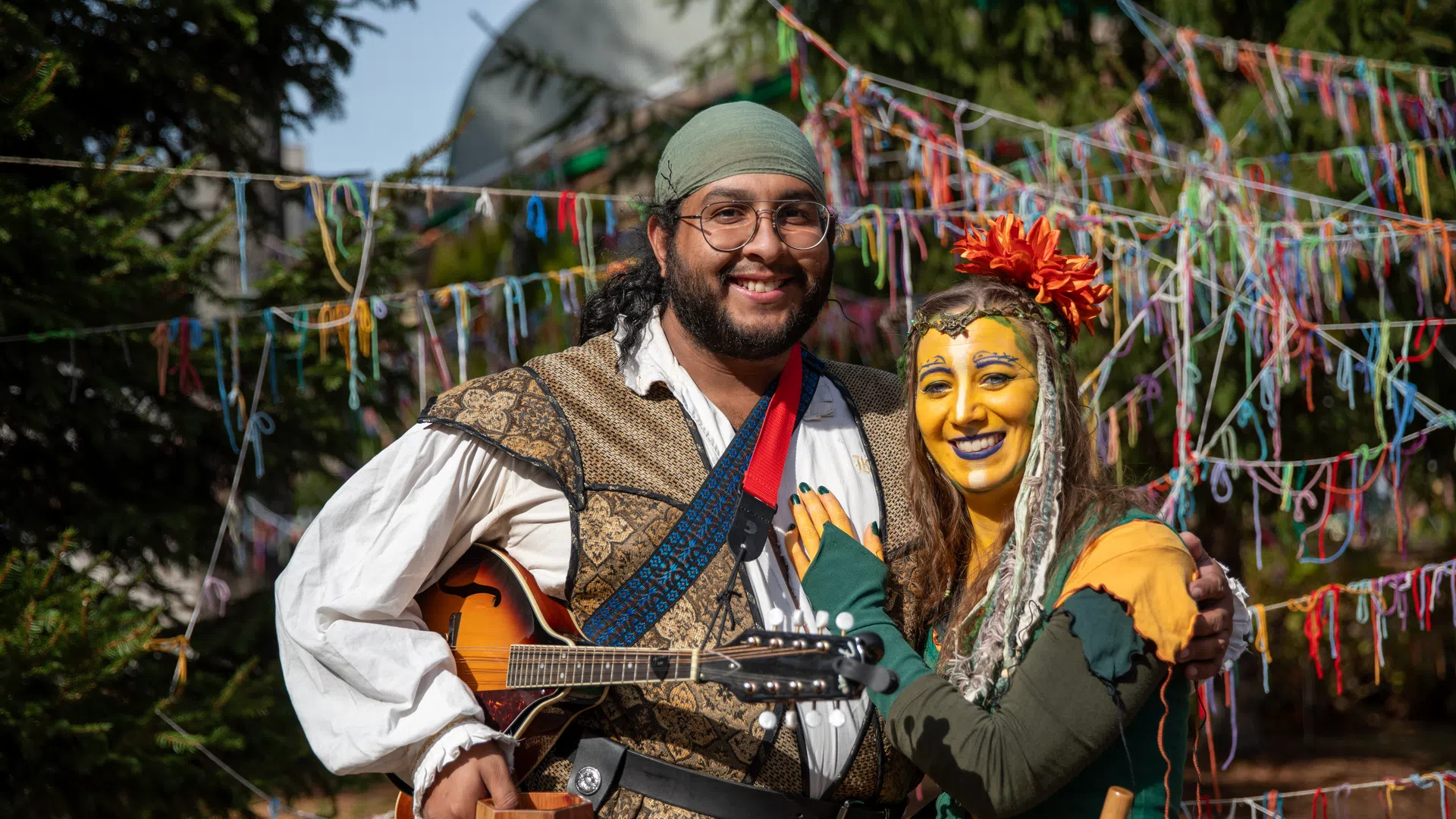 Couple in Renaissance fair costumes with colorful ribbons and outdoor festival setting in bright daylight