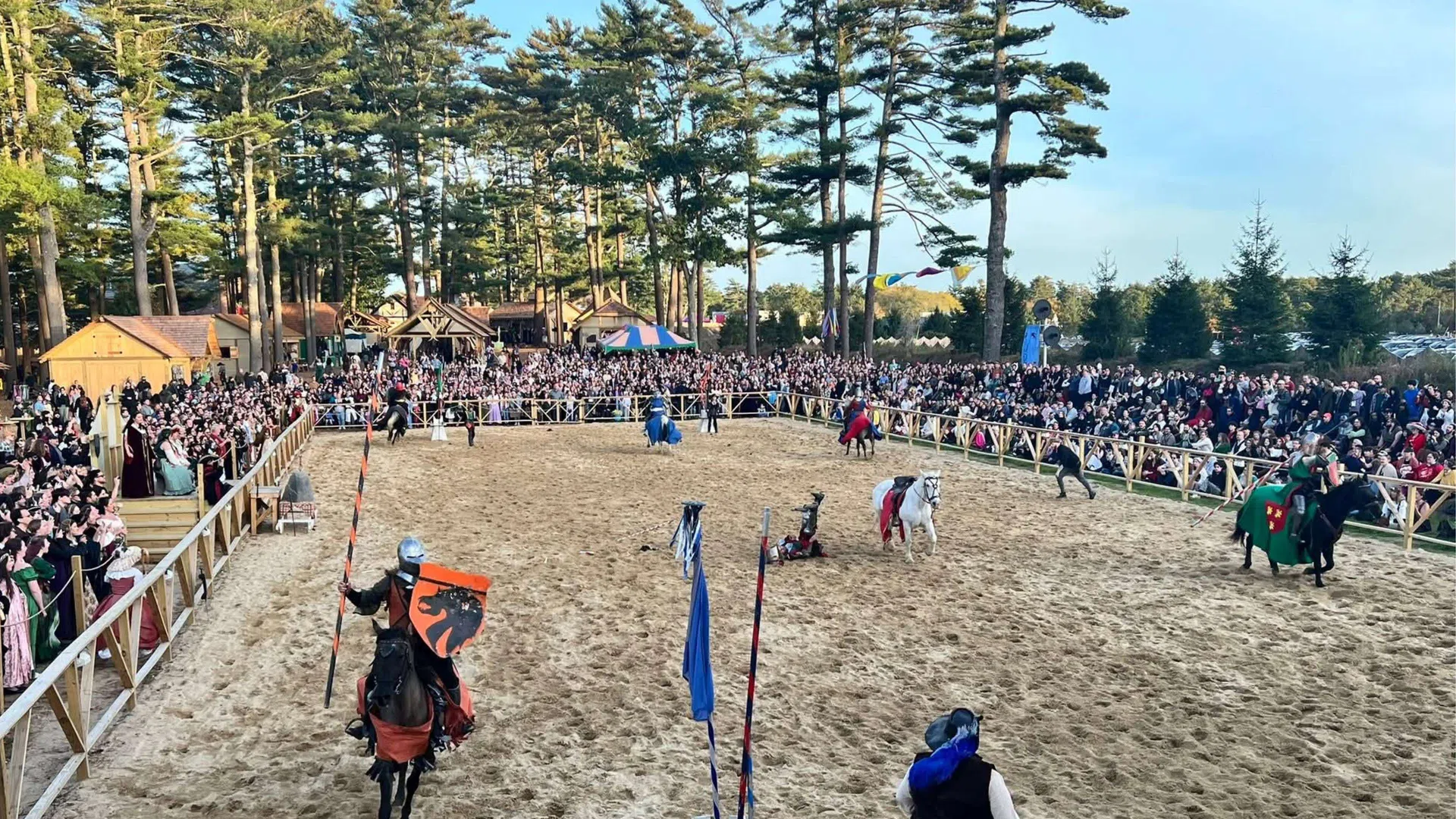 Medieval jousting tournament with knights in armor on horseback and large crowd watching outdoors