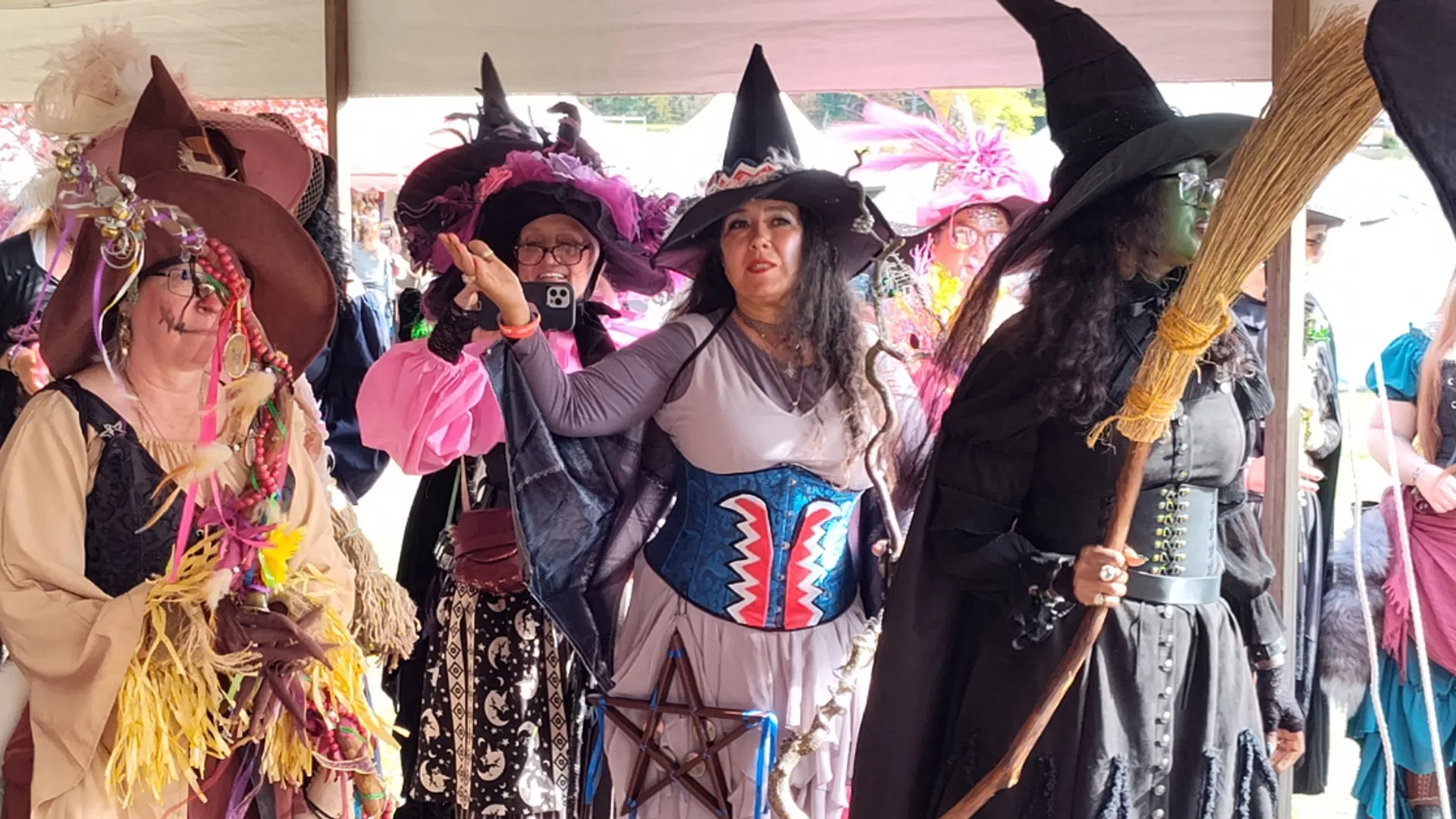 Group of women dressed as colorful witches with hats, brooms, and festive costumes at an outdoor event