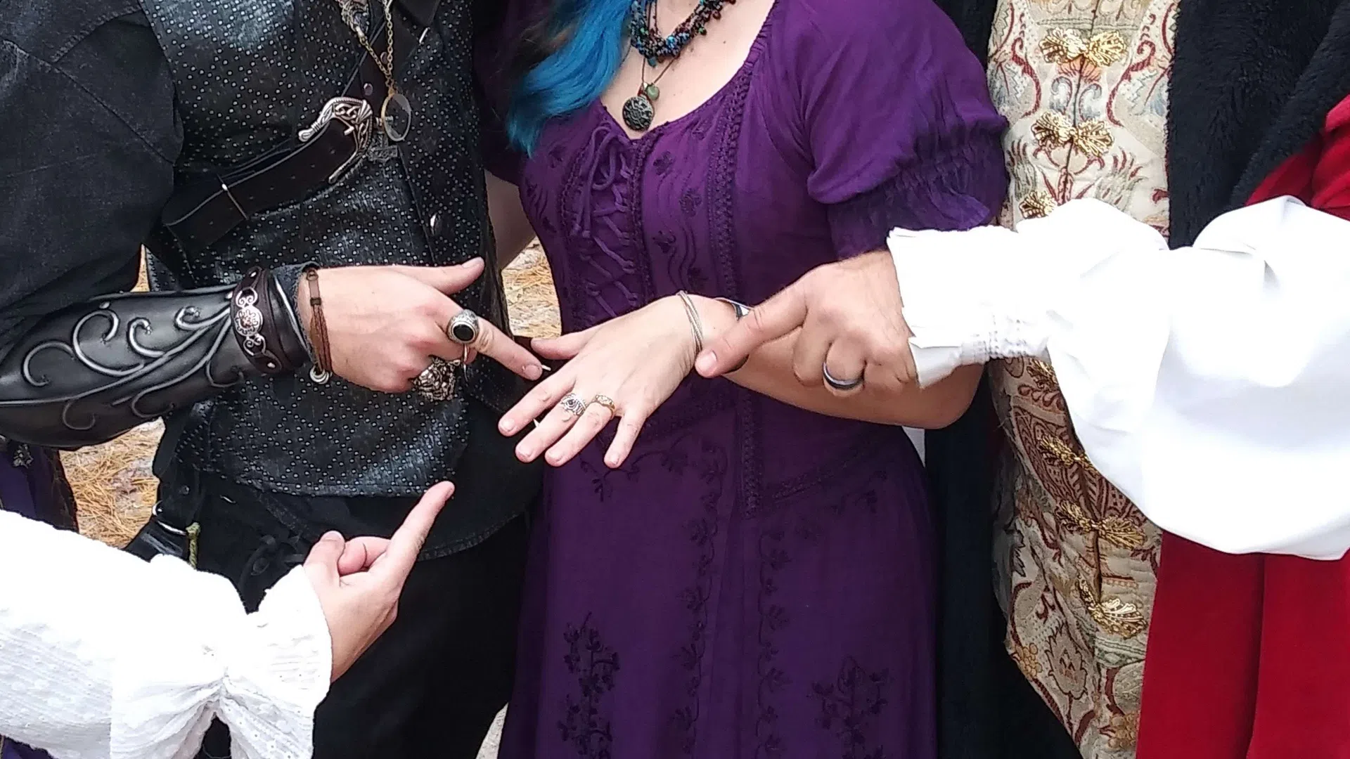 Three people in medieval costumes smiling and pointing at a woman's ring at an outdoor festival.
