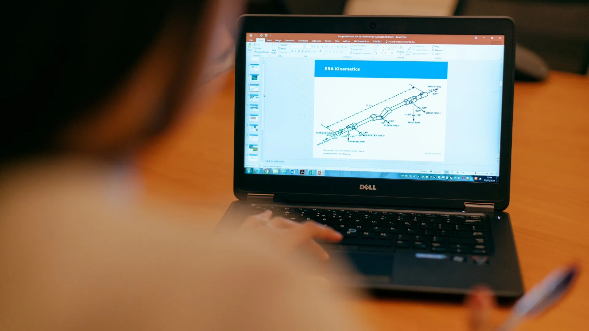 Person viewing a technical diagram labeled ERA Kinematics on a Dell laptop screen in an office setting