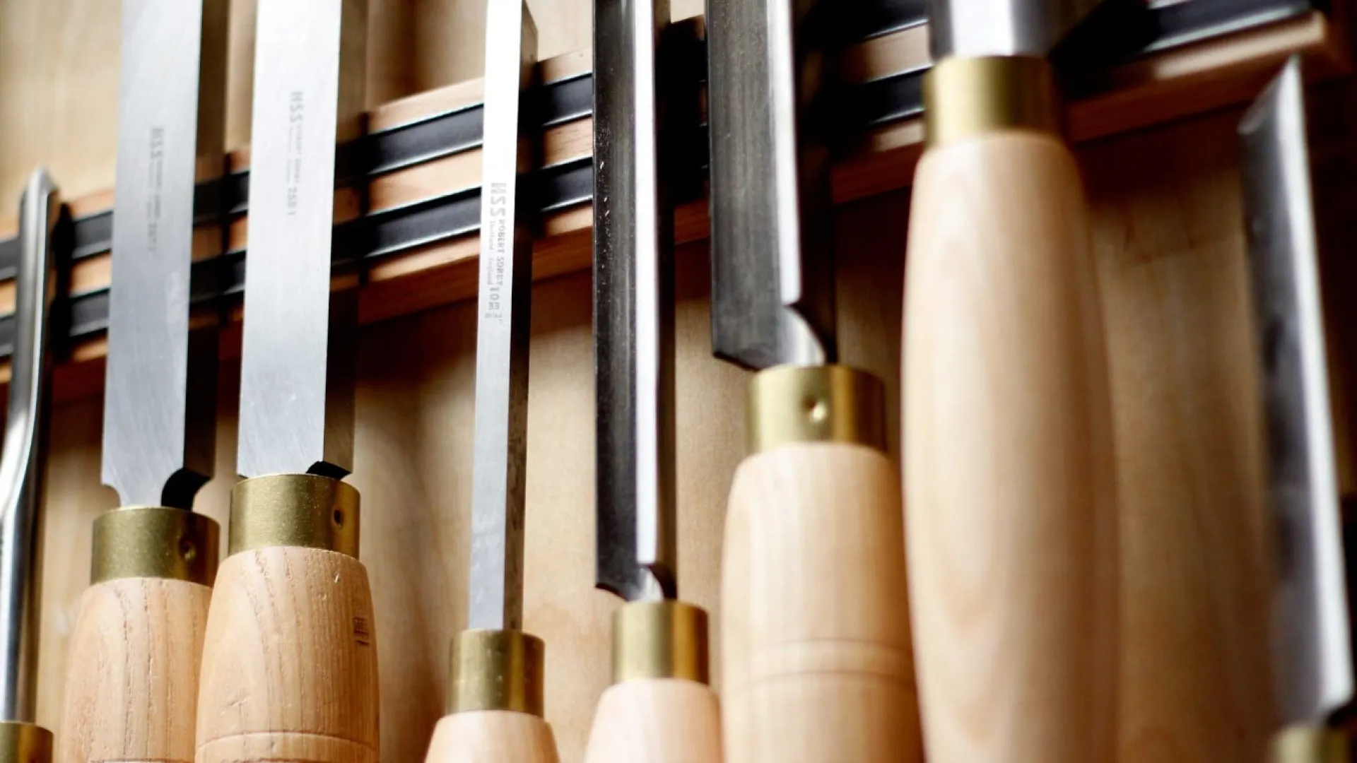 Set of woodworking chisels with wooden handles arranged on a magnetic steel strip against a wooden background.