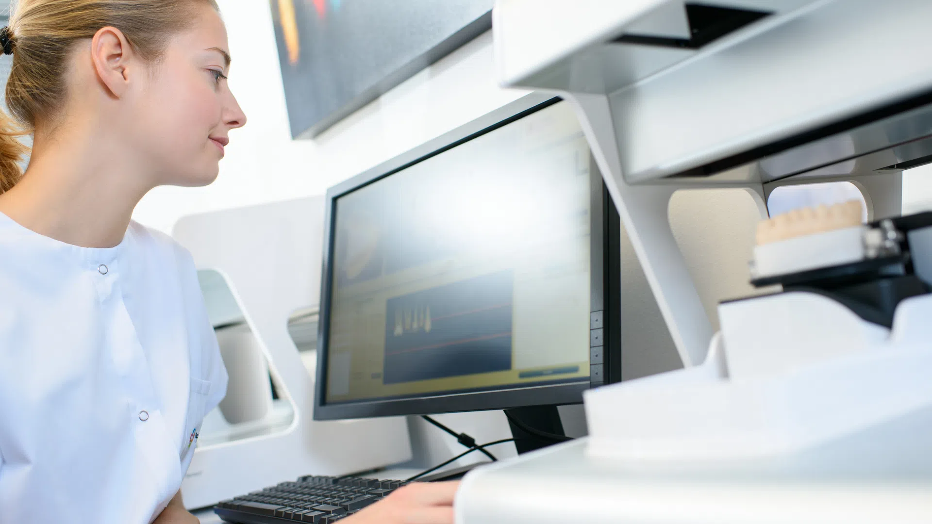 Female technician using dental CAD software on computer in modern dental laboratory
