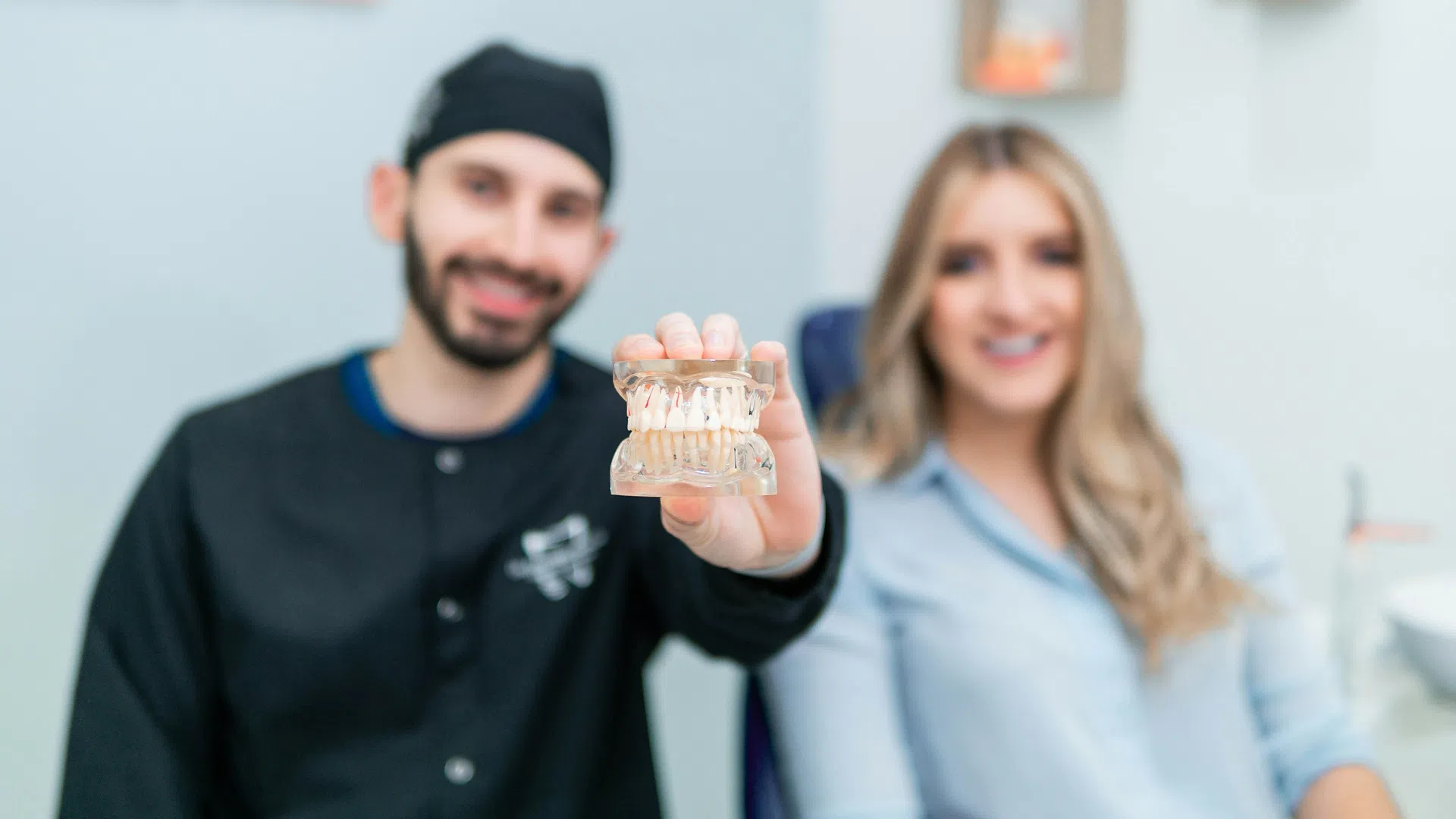Dentist holding a dental model with a smiling patient in the background in a dental clinic.