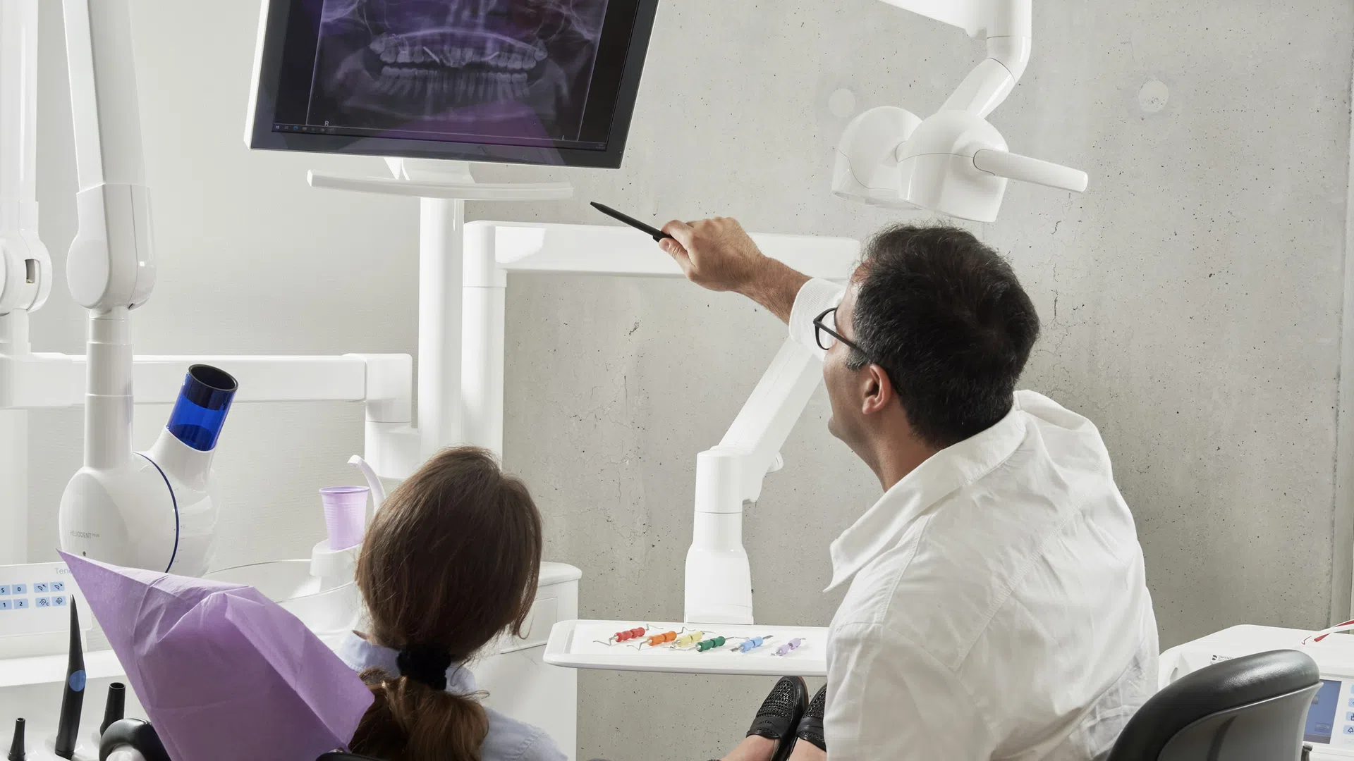 Dentist explaining a dental X-ray on screen to a female patient in a modern clinic.