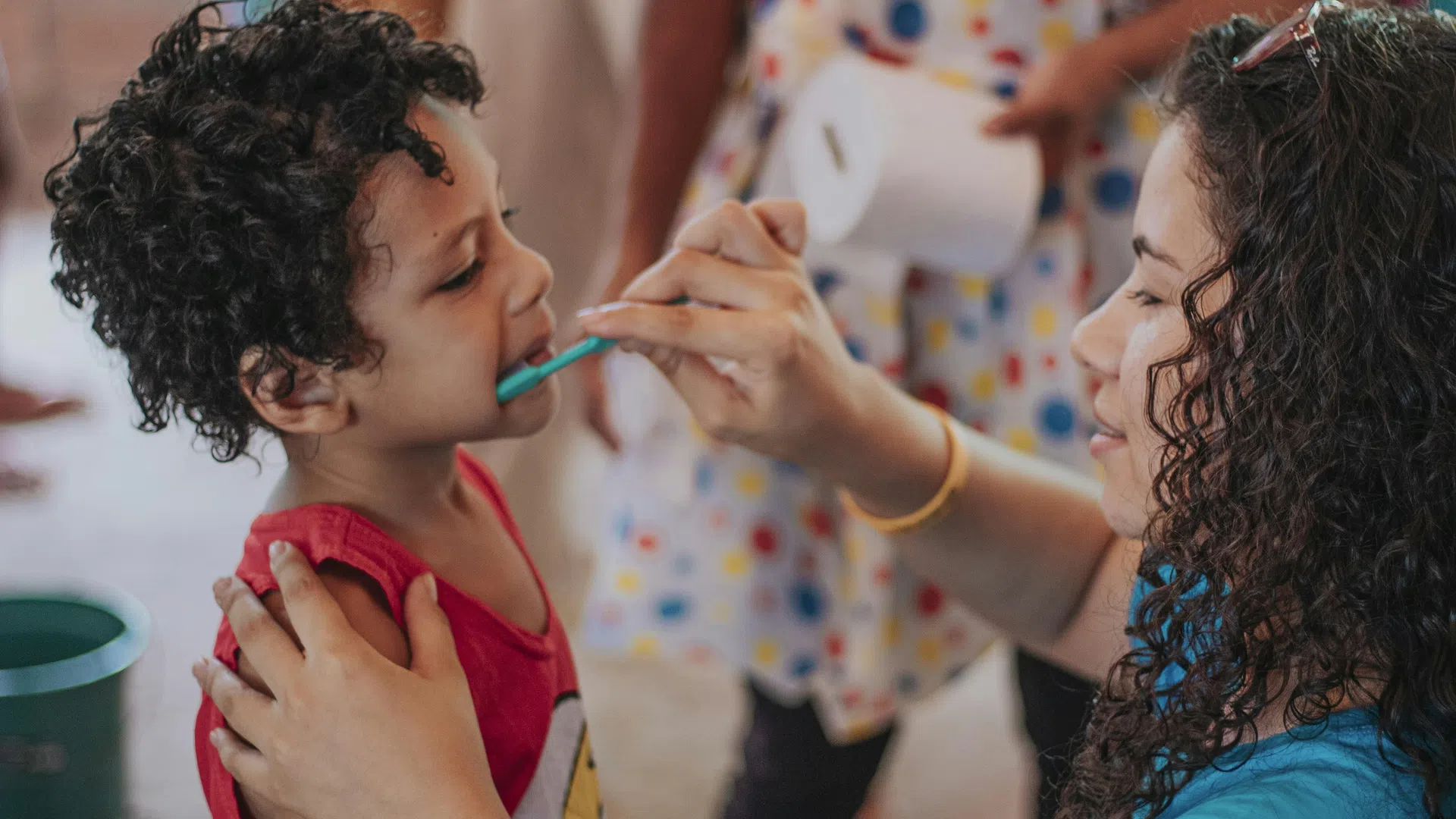 Woman helping young boy brush teeth with a toothbrush indoors, promoting dental hygiene for kids.