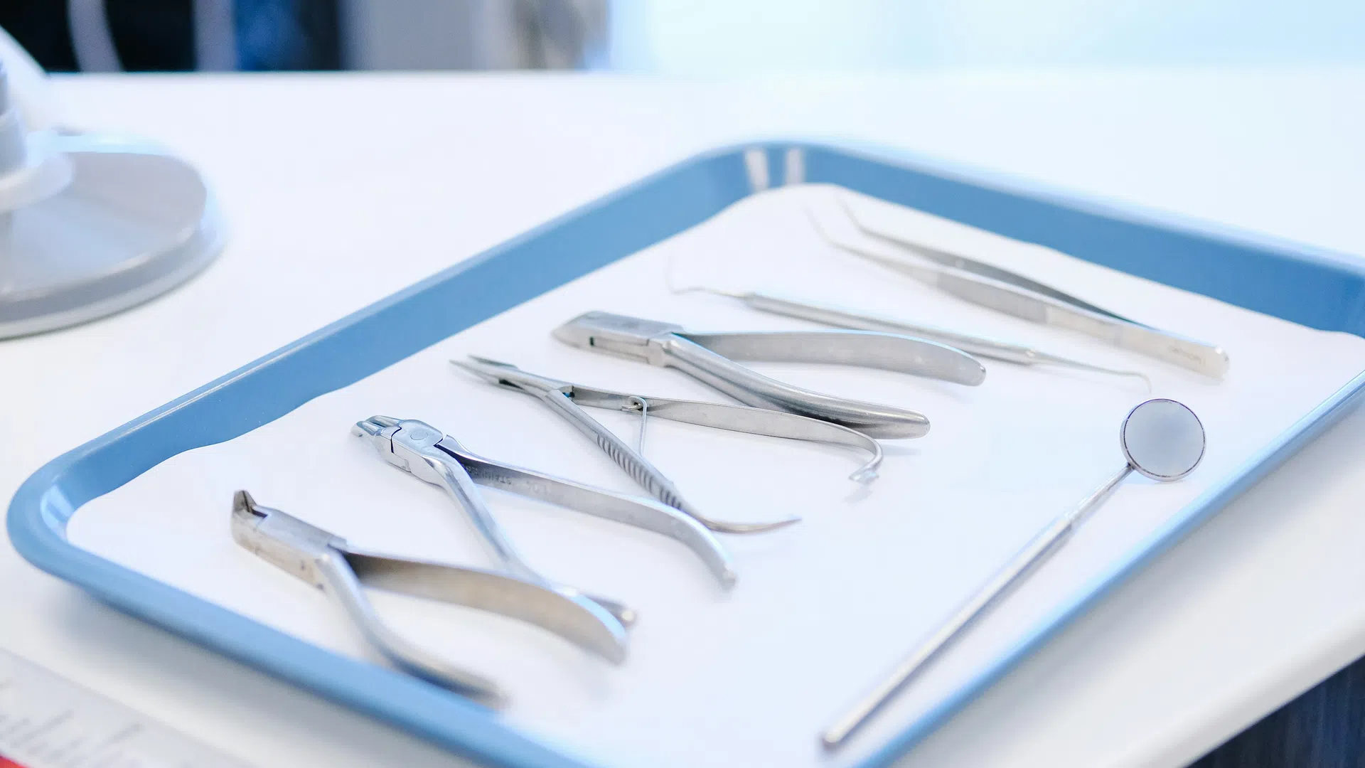 Dental tools including pliers, mirror, and tweezers arranged on a blue tray in a clinical setting