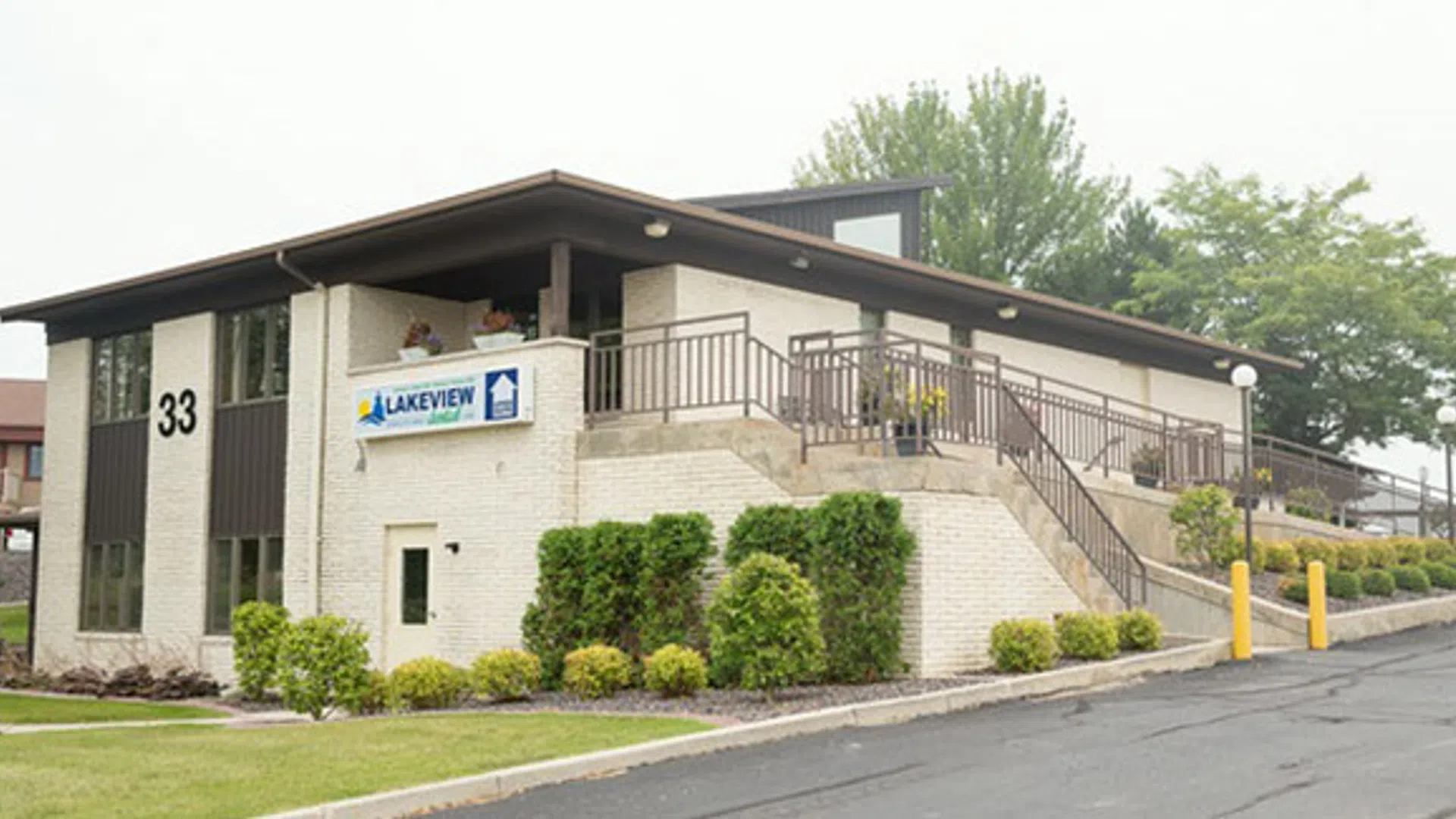 Modern two-story Lakeview building with stairs, railings, greenery, and a parking lot under an overcast sky