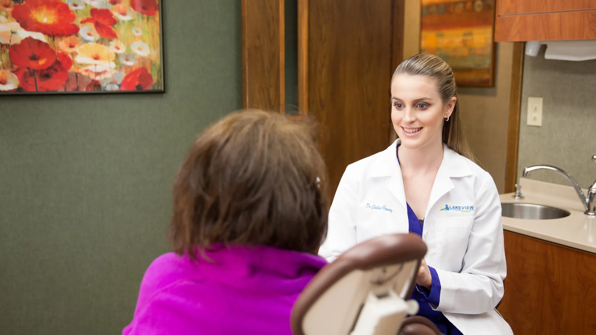 Female doctor in white coat smiling and talking to patient wearing purple in medical office
