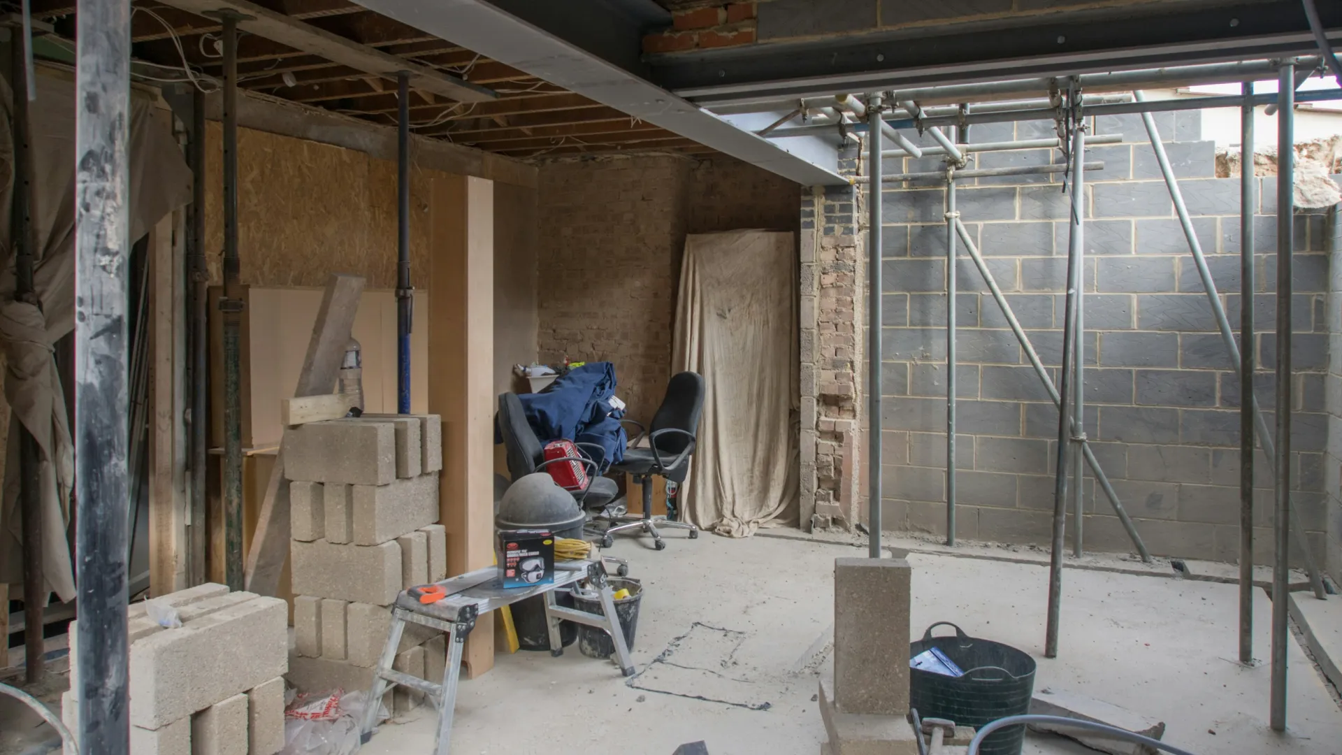 Interior view of a construction site with tools, bricks, and scaffolding in a partially built room.