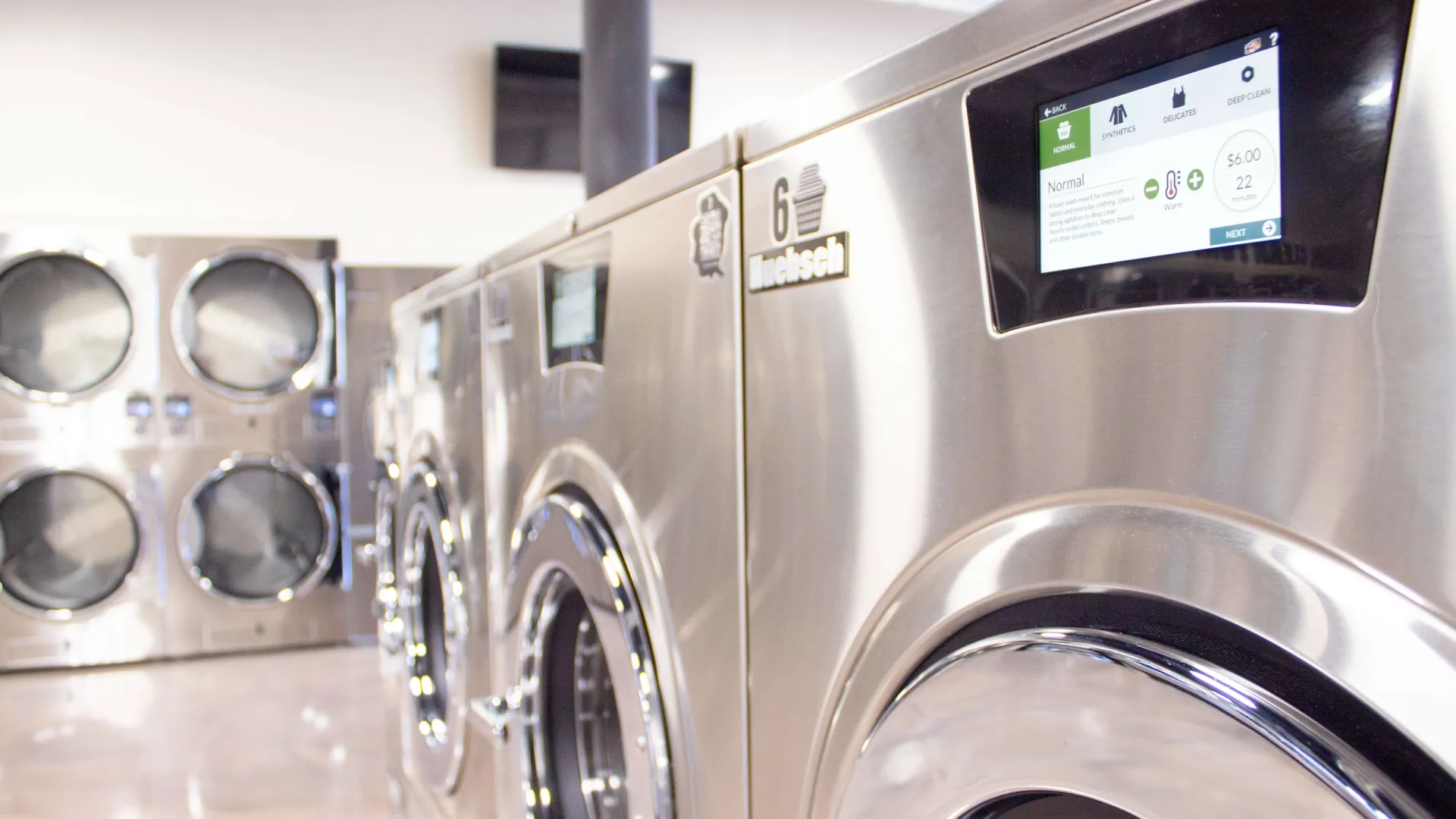 Row of modern industrial washing machines with digital displays in a bright laundry facility.
