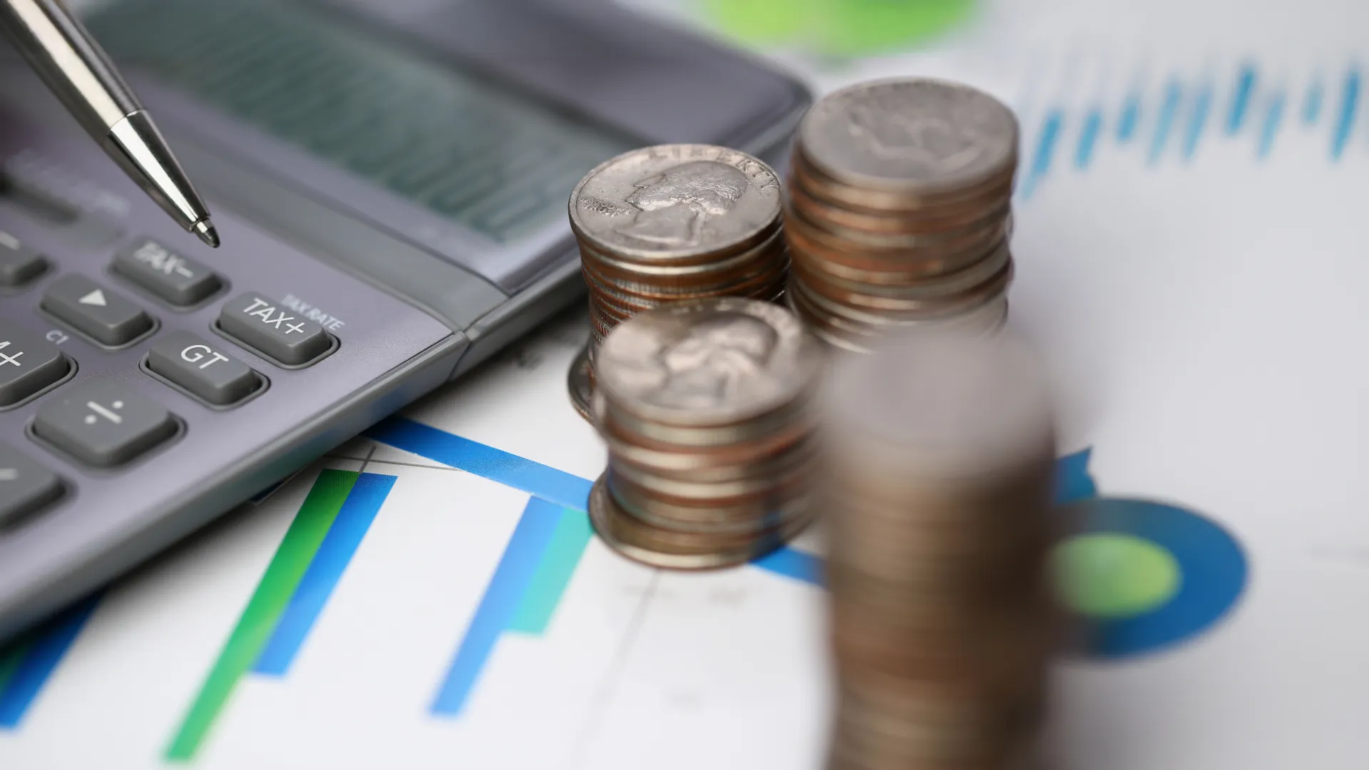 Stacks of coins next to a calculator and pen on financial charts depicting investment and budgeting concepts