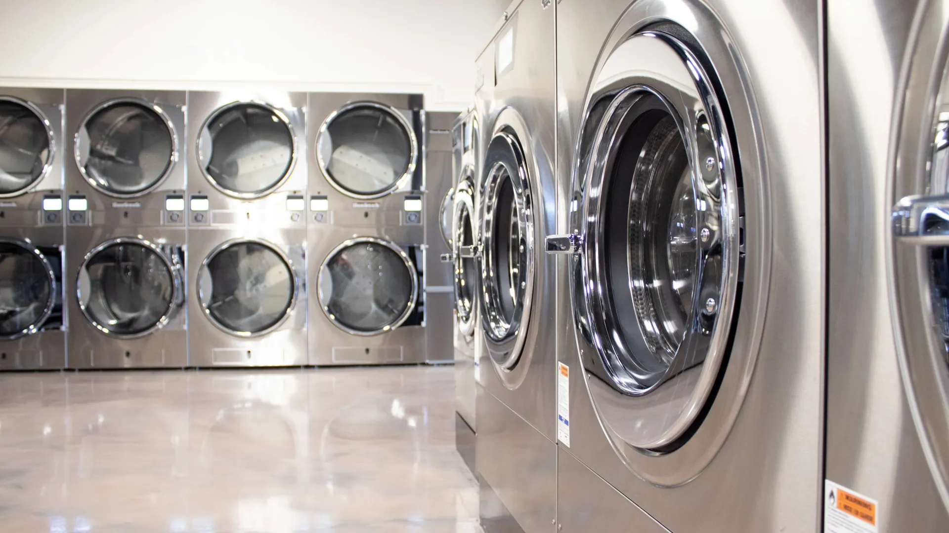 Man sitting and using phone while woman loads laundry into washing machine in laundromat