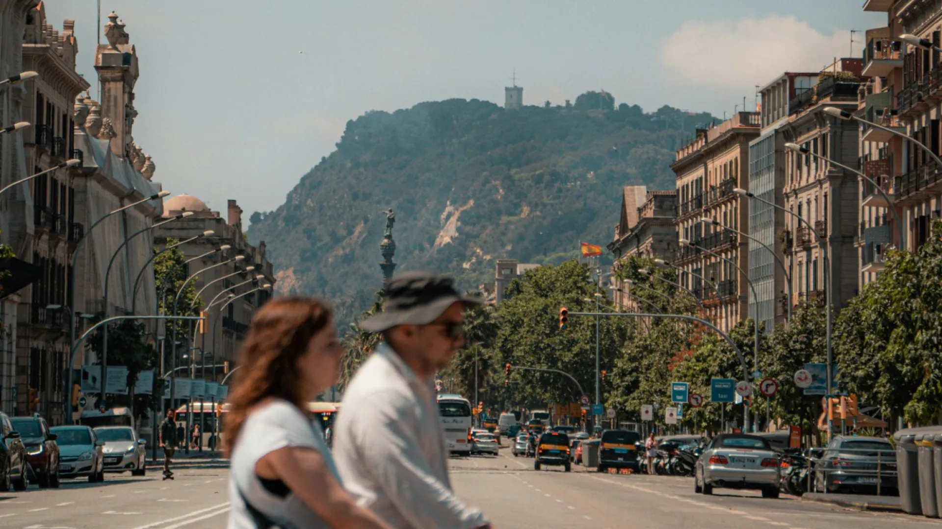 Family crossing a busy city street with mountains and historic buildings in the background under blue skies