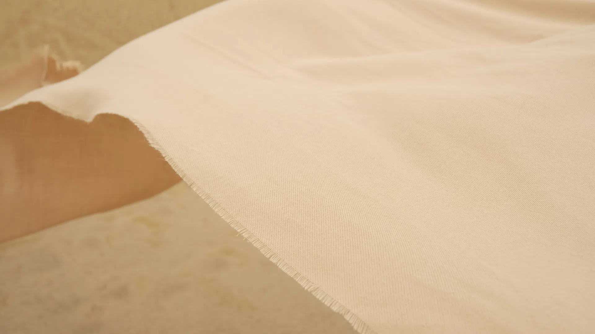 Light beige fabric with a smooth texture and frayed edge draped over a neutral background.