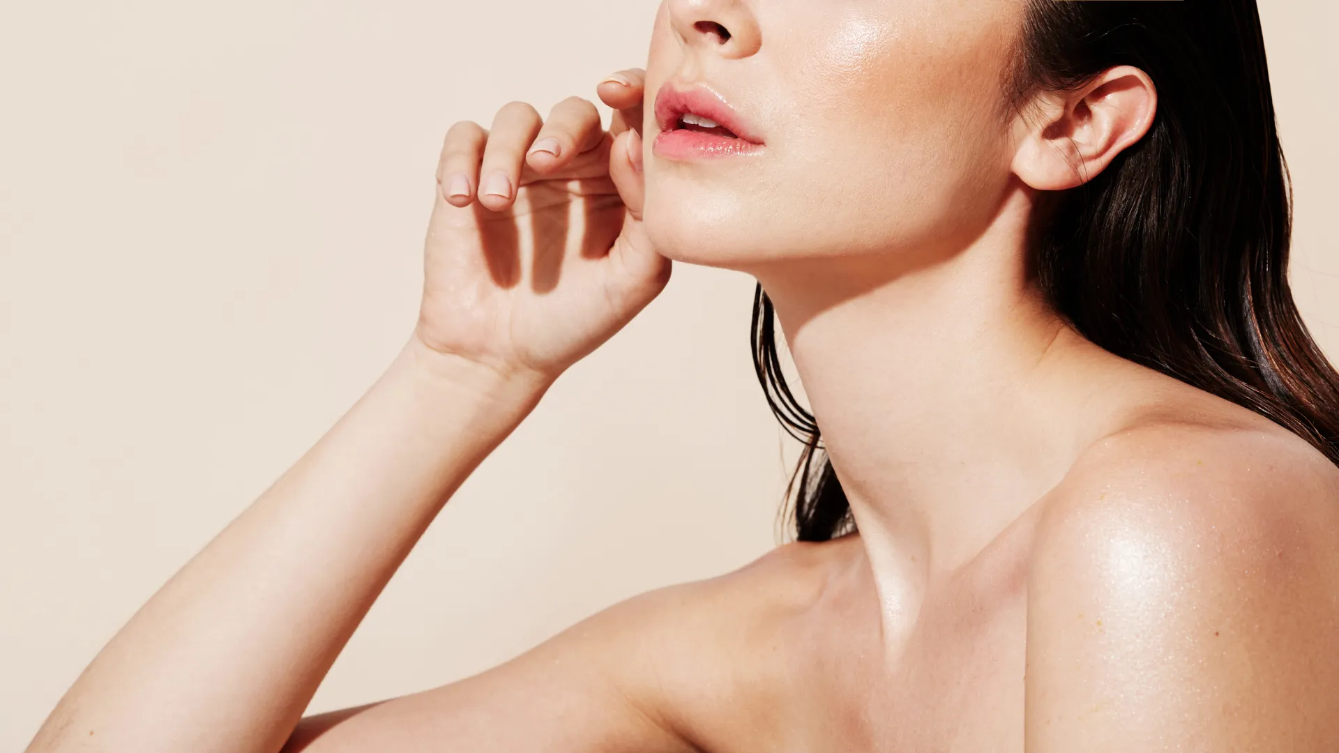 Close-up of a woman with smooth skin, glossy lips, and dark hair against a beige background