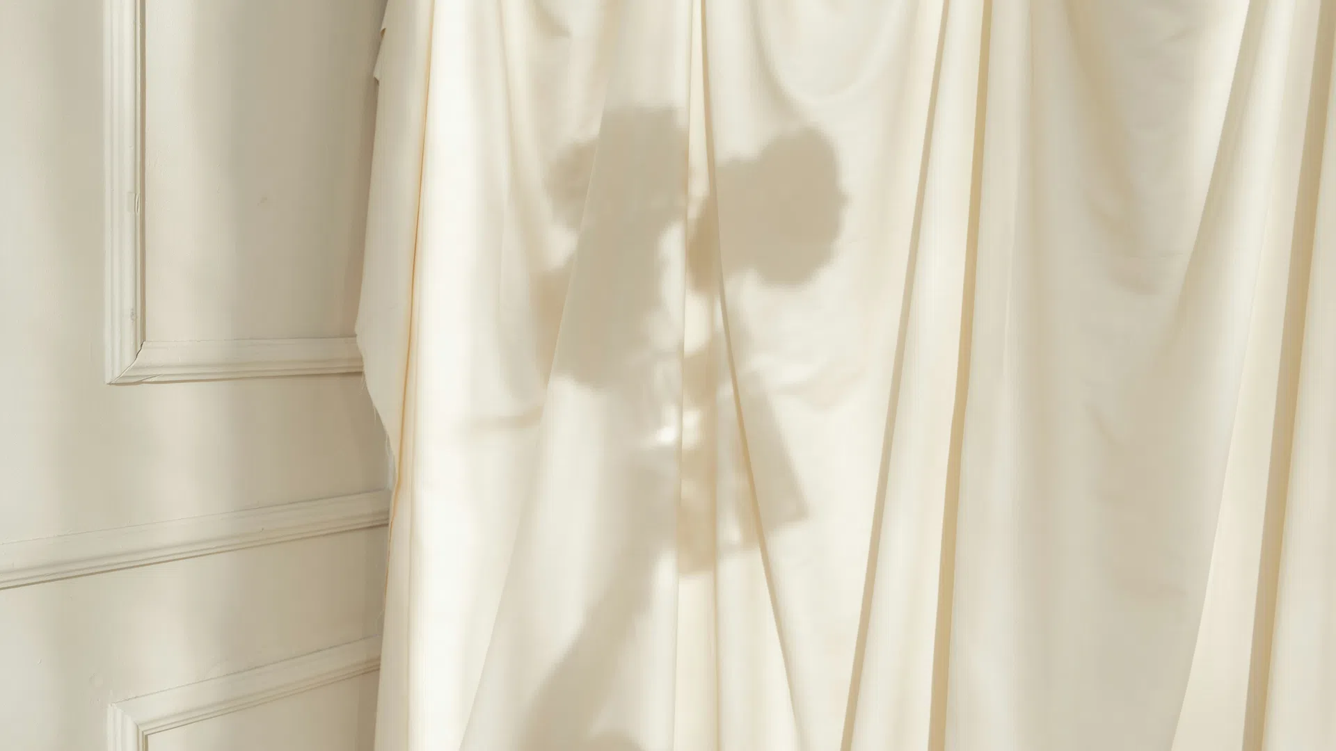 Shadow of a person with curly hair cast on cream-colored curtains in a softly lit room.