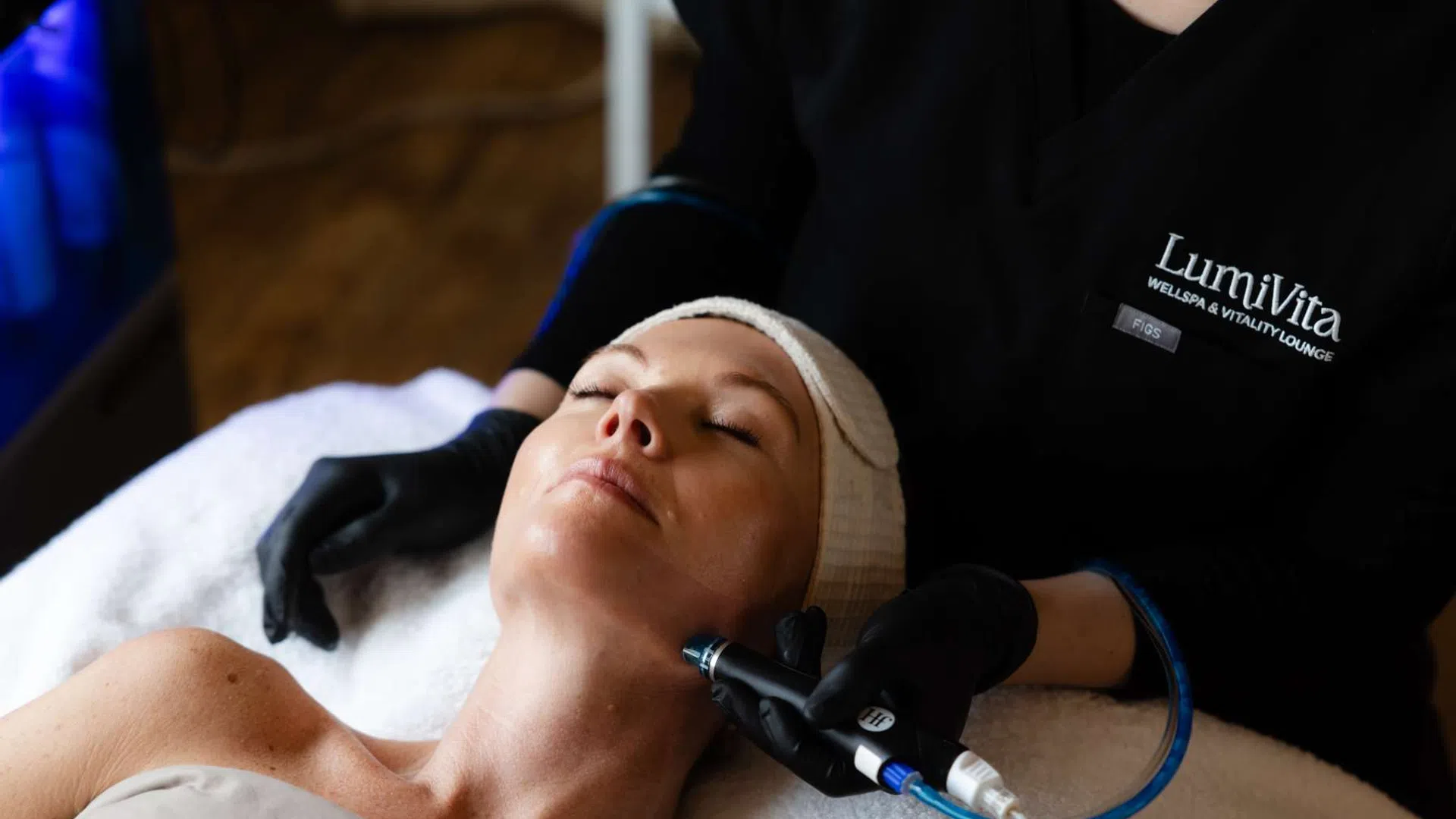 Woman receiving a facial treatment with a handheld device at LumiVita wellness spa and vitality lounge.