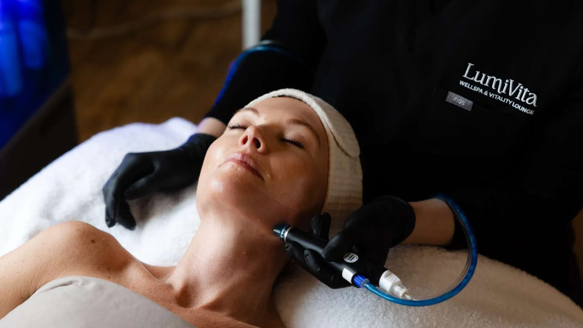 Woman receiving a facial treatment with a handheld device at LumiVita wellness spa and vitality lounge.