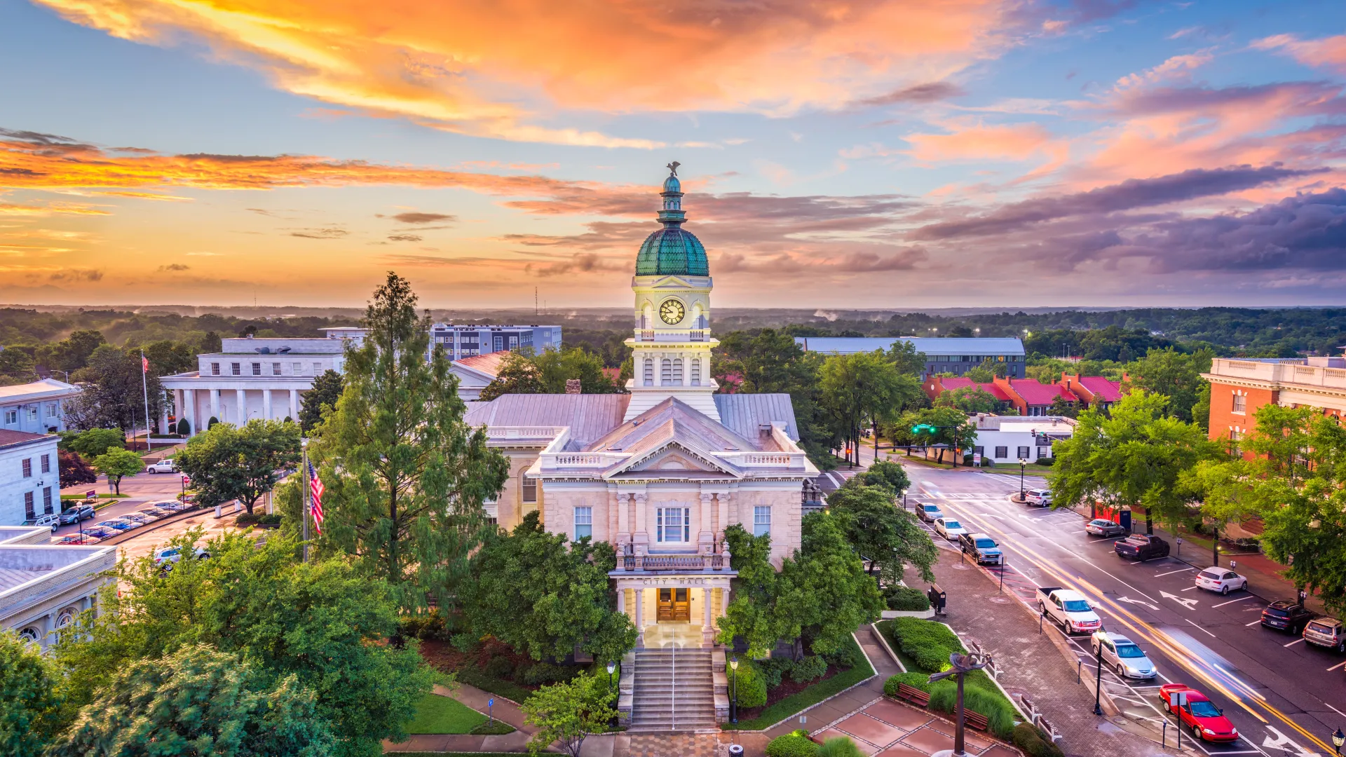 Historic courthouse with clock tower at sunset in a small town surrounded by trees and streets with cars.