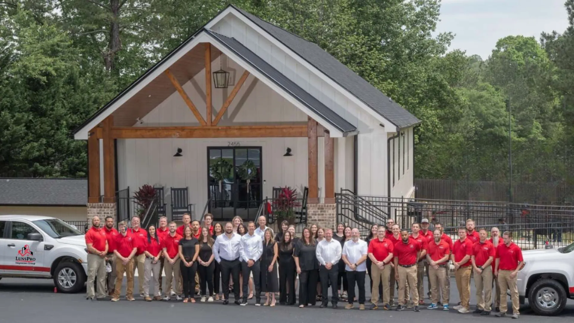 Large group of professionals standing in front of a modern office building with company vehicles on both sides.