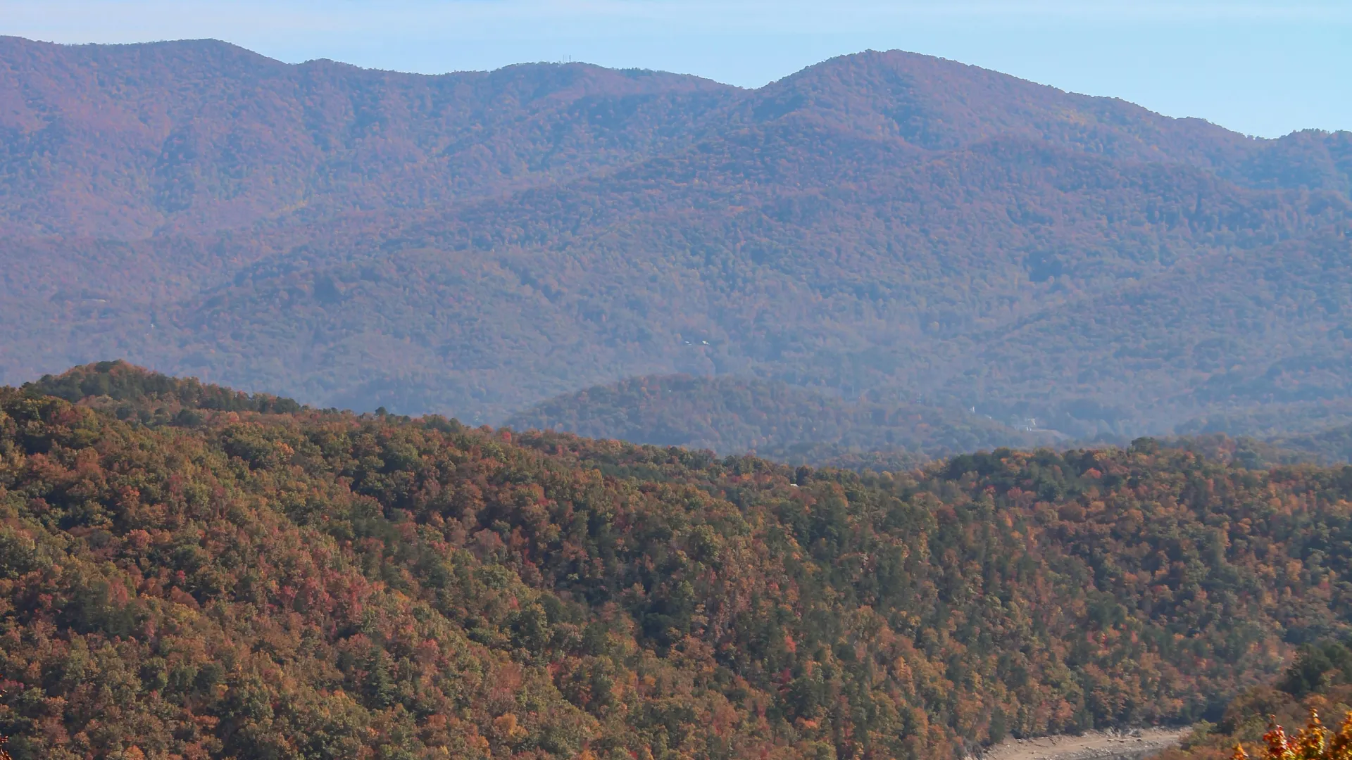 Scenic river winding through autumn-colored forested hills under a partly cloudy blue sky.
