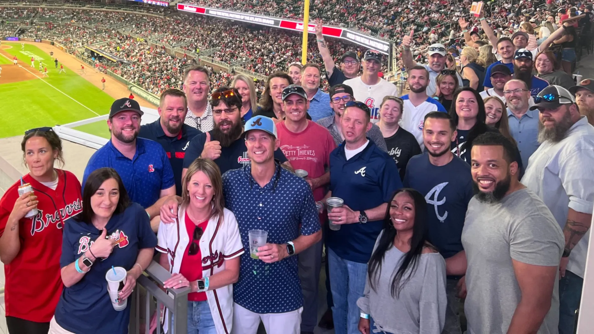 Group of fans enjoying a baseball game at a crowded stadium with bright lights and field view.