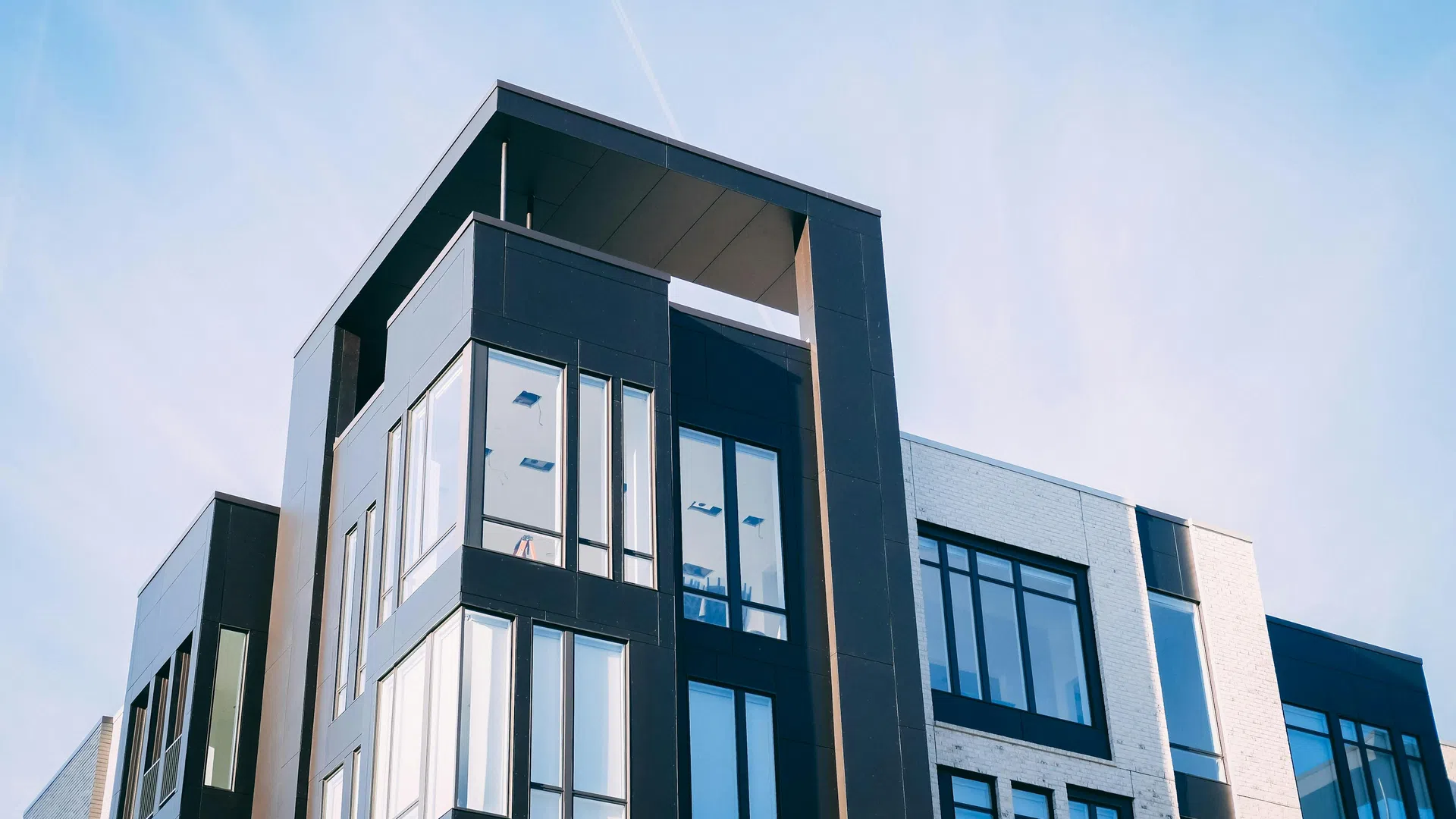 Modern multi-story building with large glass windows and black exterior elements under a clear blue sky.