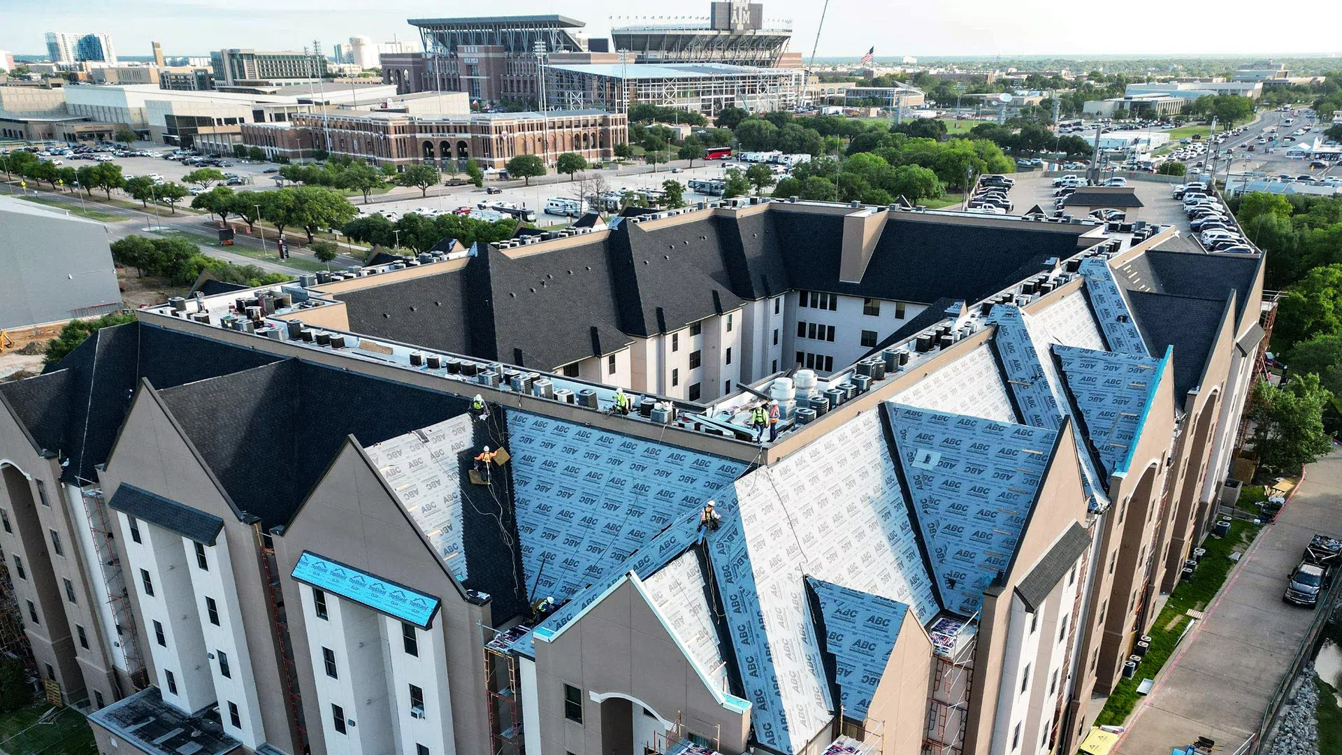 Aerial view of a large multi-story building under roof construction with workers and materials on the rooftop