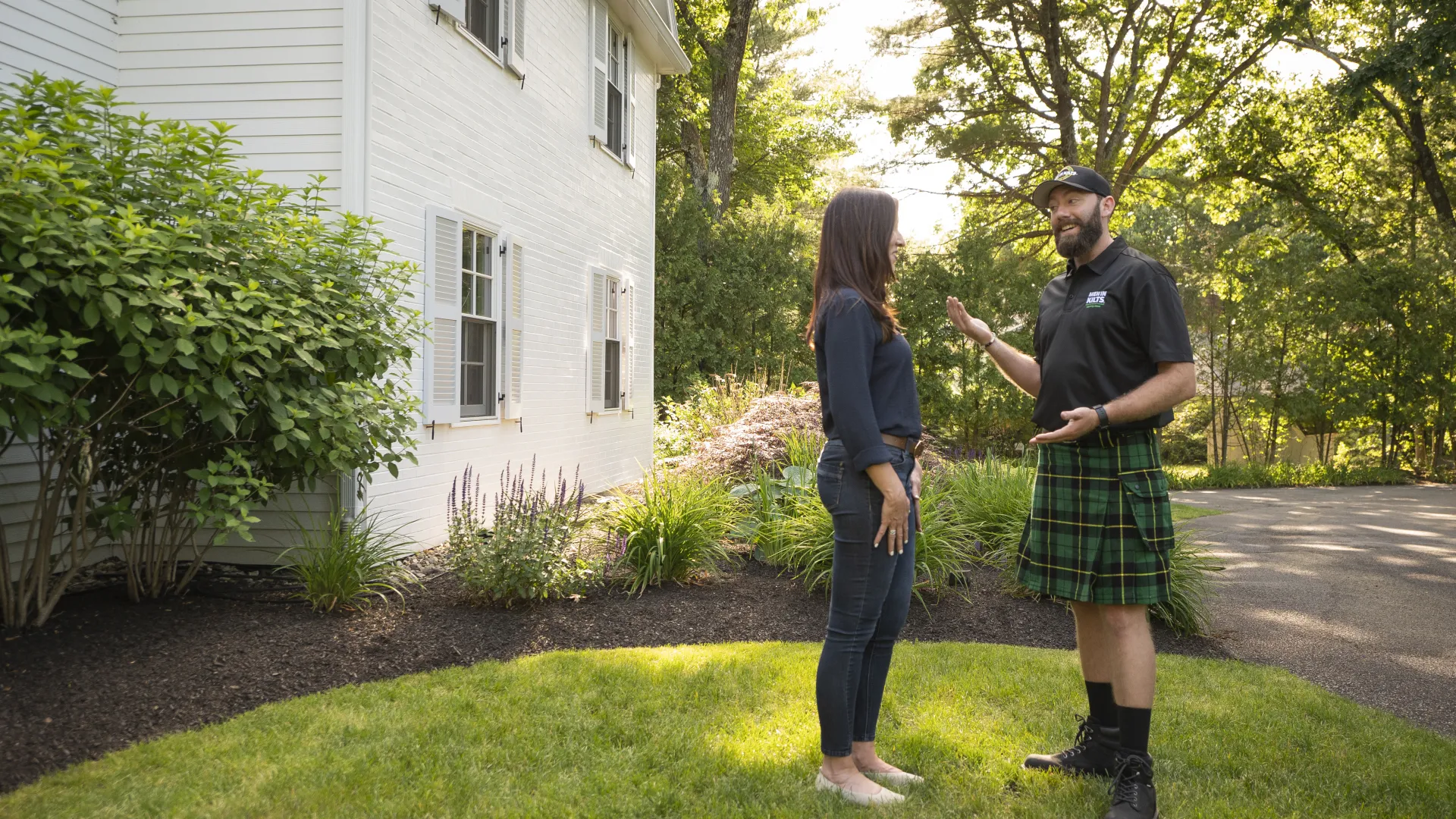 a man and a woman standing in a yard with a house and trees