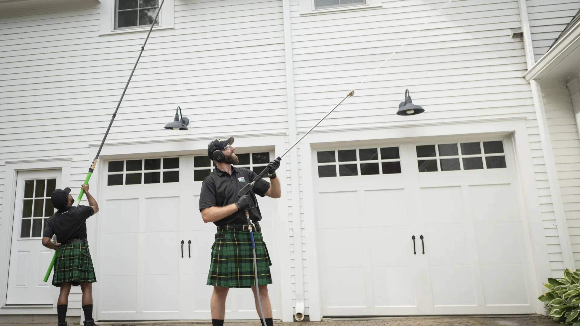 a person in a kilt holding a pressure washer in front of a white house