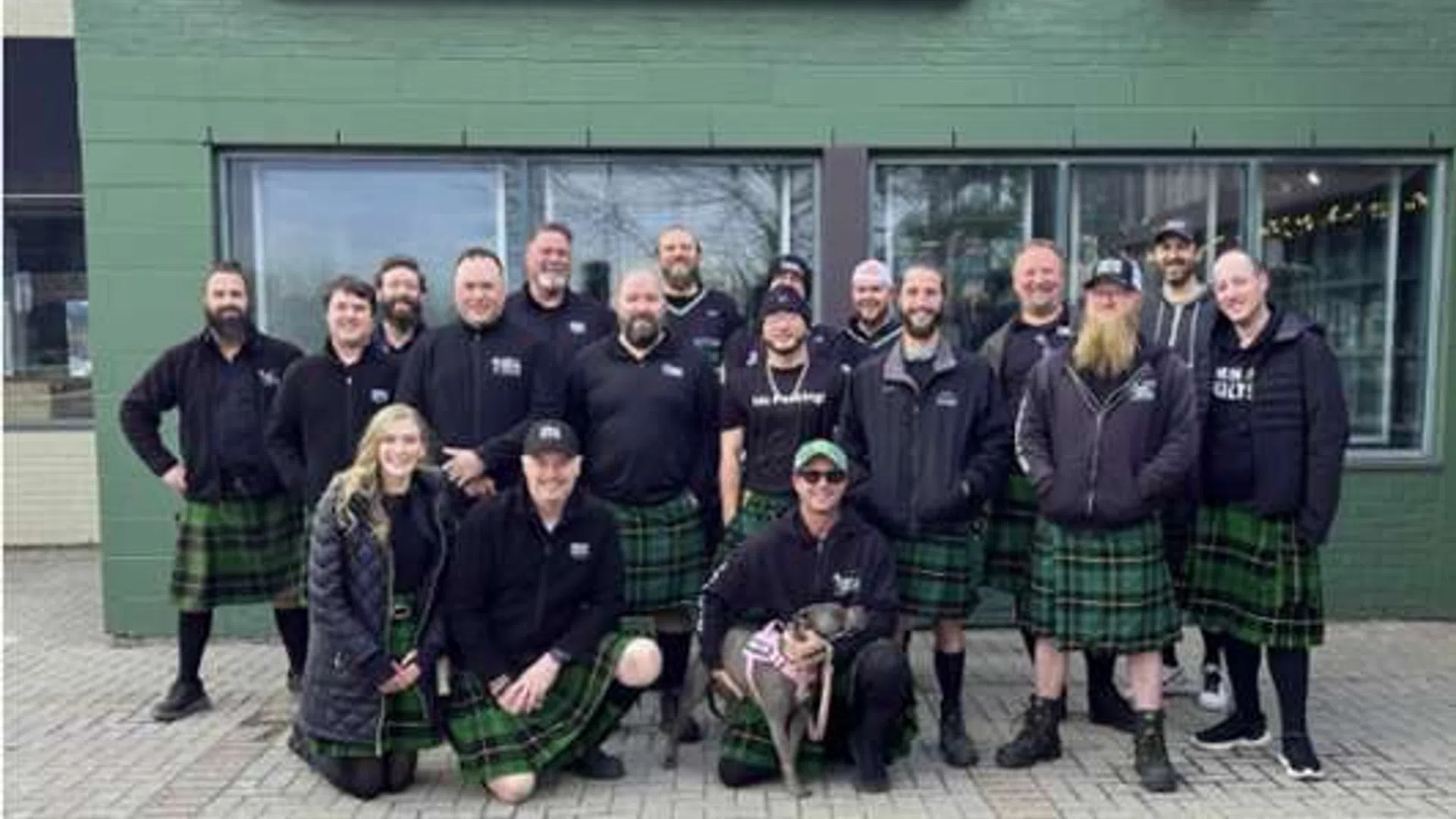Group of people wearing kilts posing outside Fionn Maccool's restaurant and pub with green exterior wall.