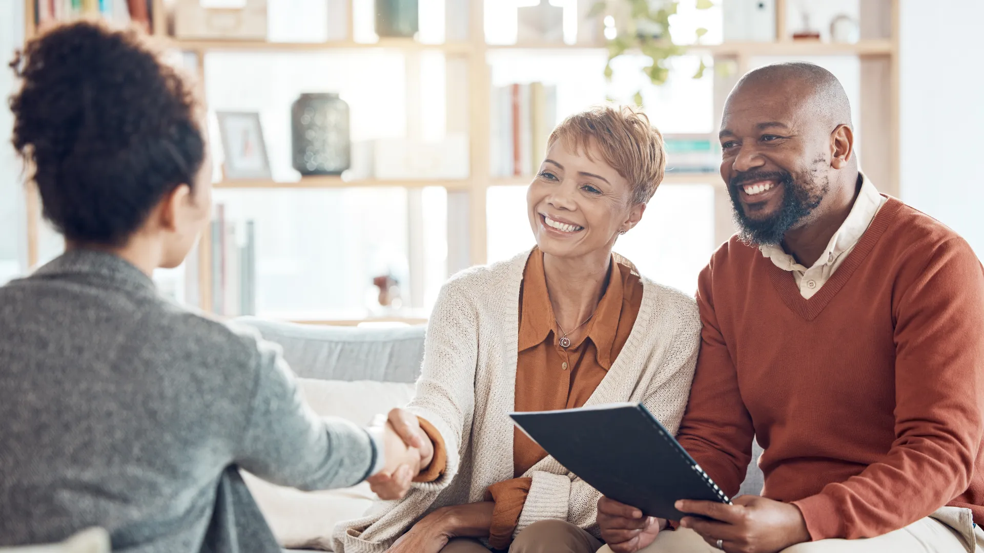 Happy couple shaking hands with a professional during a friendly meeting in a bright living room.