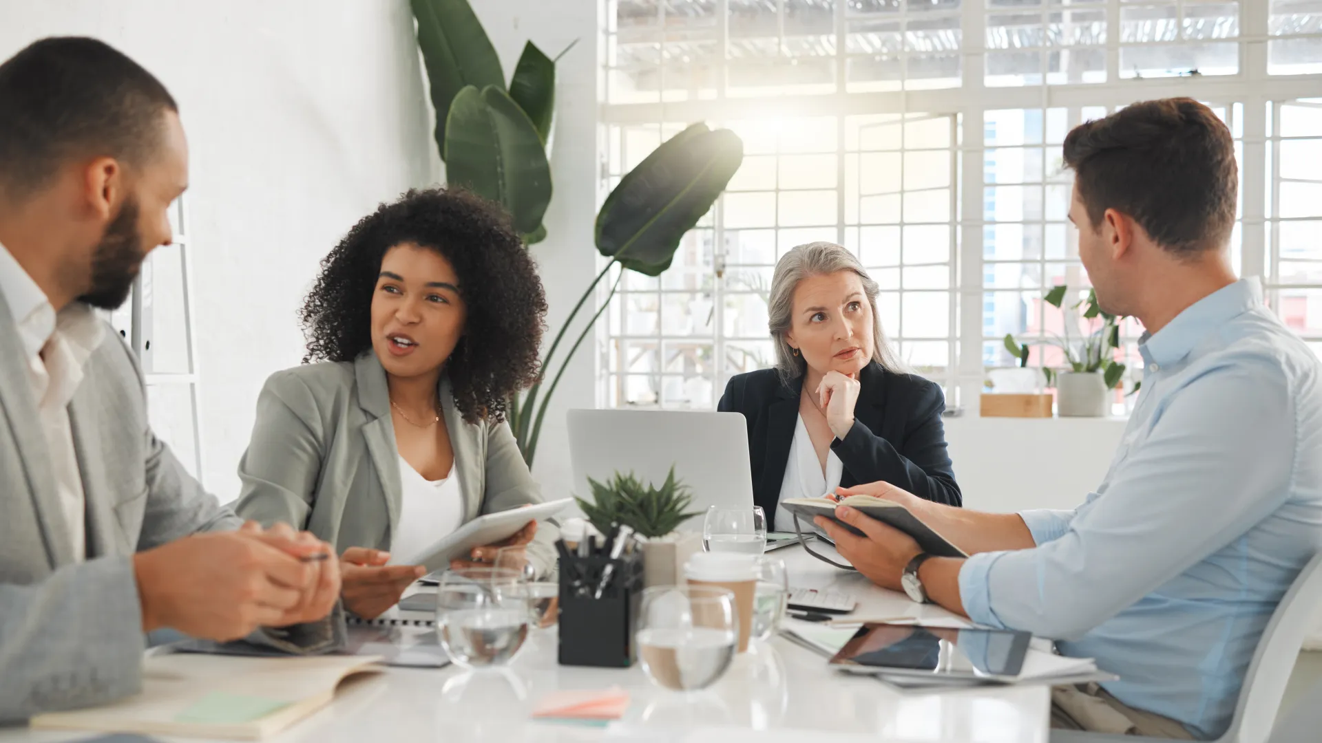 Four diverse professionals engaged in a business meeting around a white table with laptops and documents.