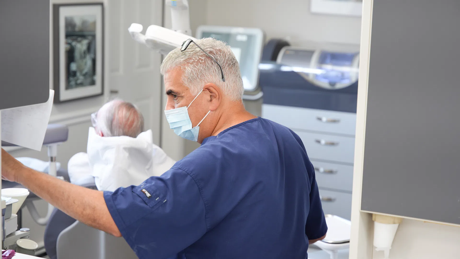 Dentist in blue scrubs and mask working with patient in modern dental clinic setting.