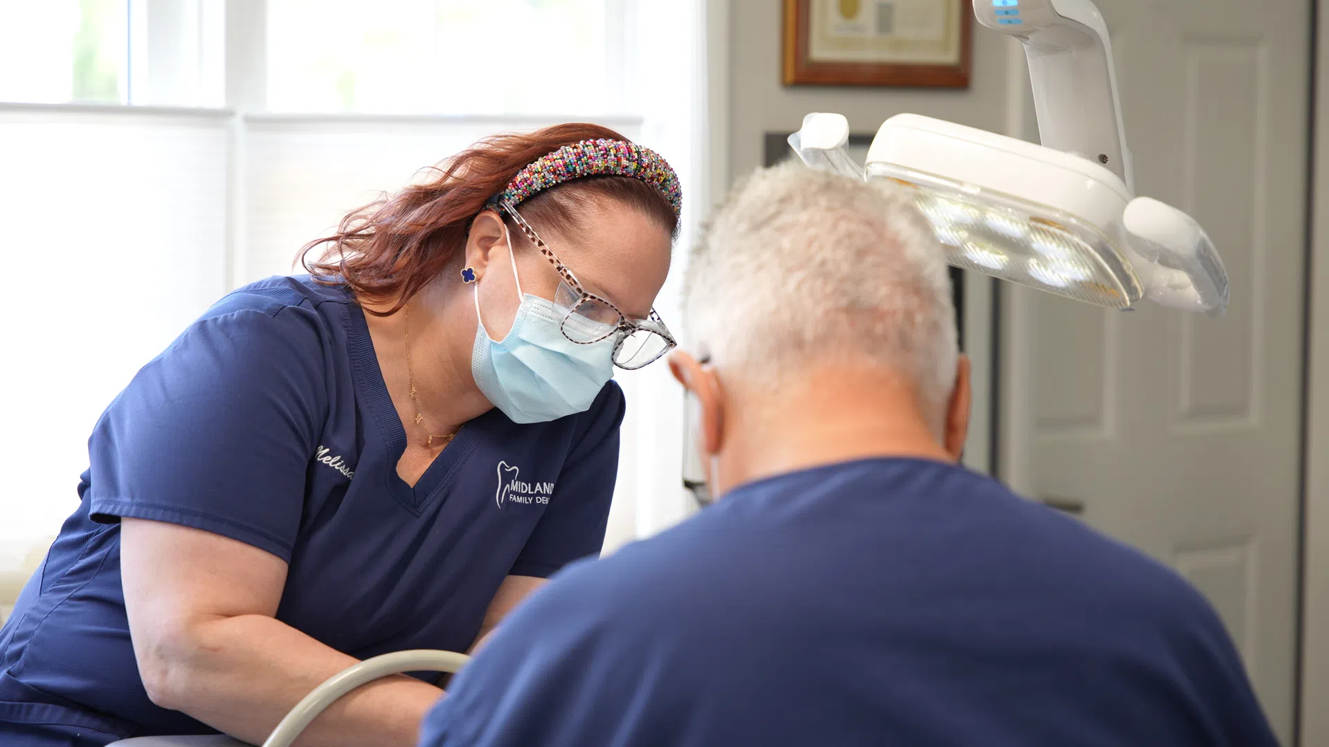 Dentist wearing mask and glasses treating elderly male patient in a bright dental clinic with equipment.