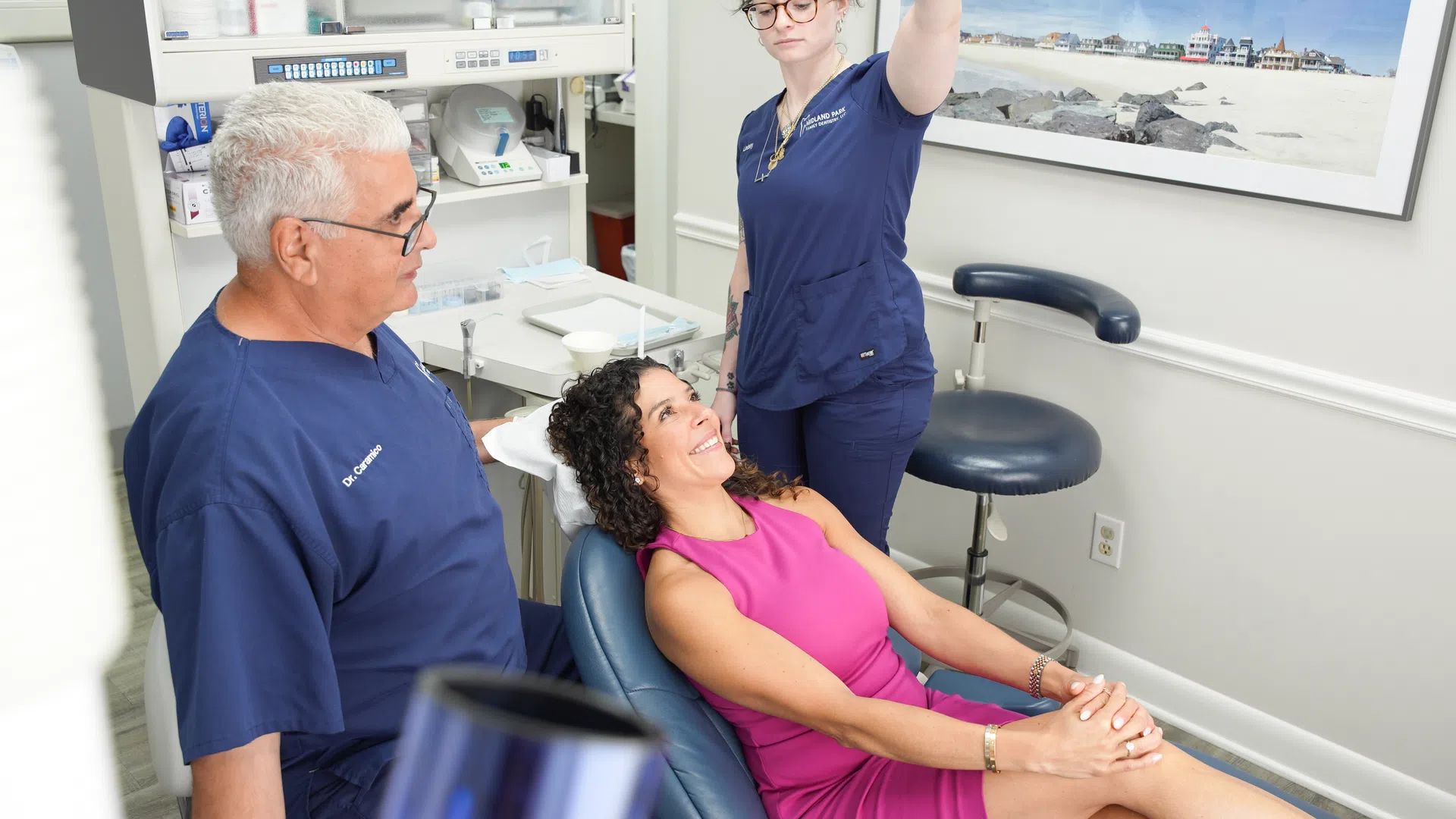 Dentist and assistant attending to a smiling female patient in a modern dental clinic room.
