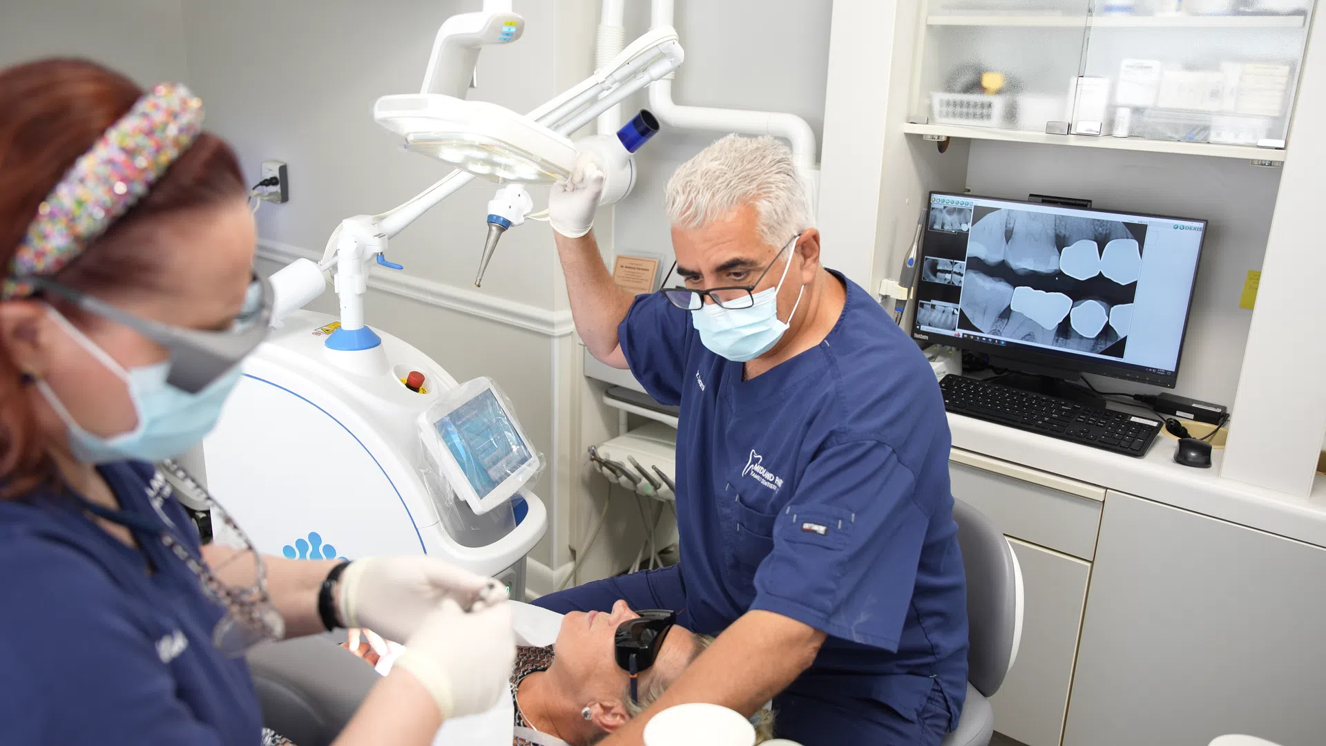 Dentist and assistant perform dental procedure using modern equipment and dental X-rays on screen