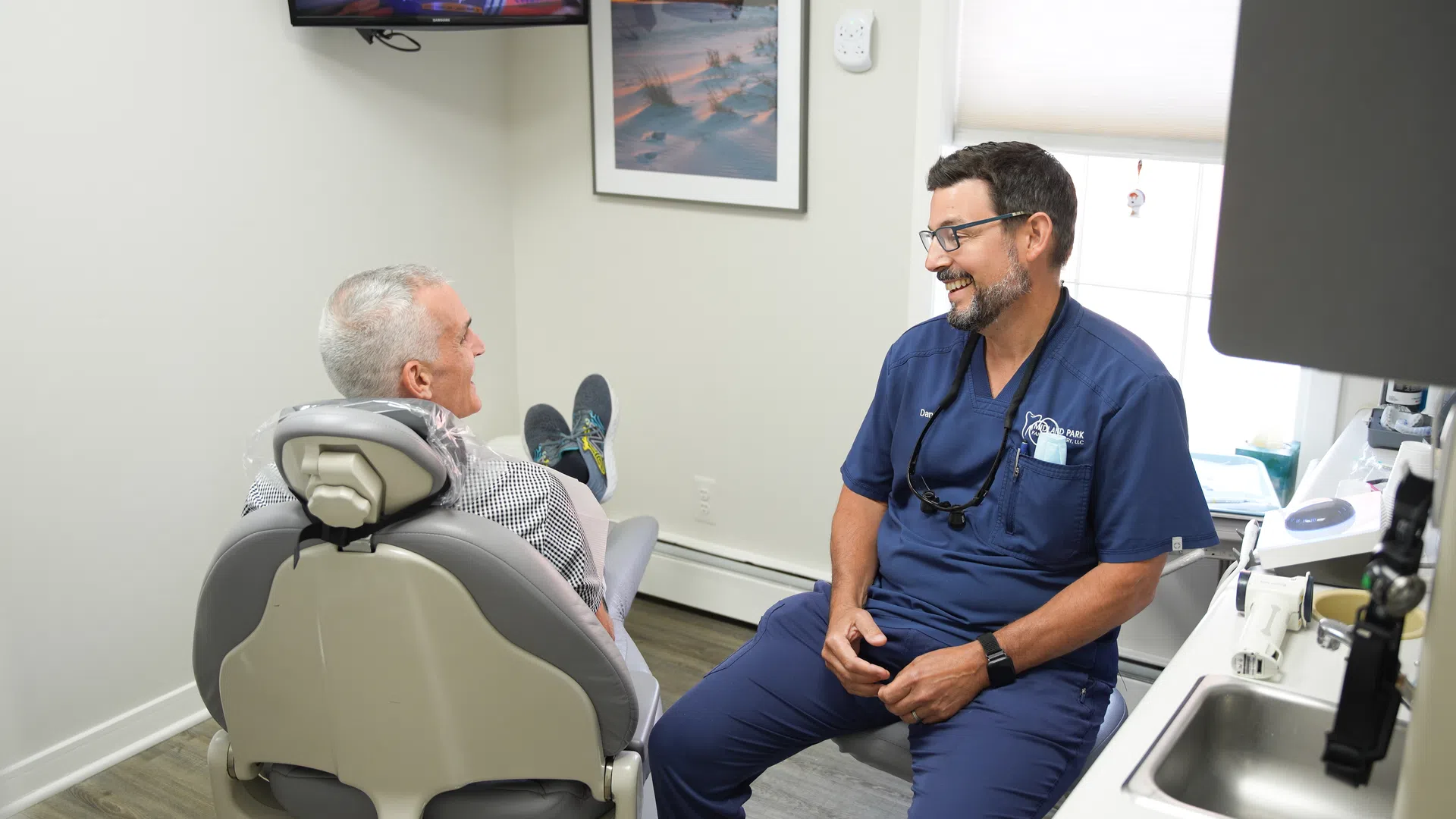 Dentist consulting and smiling with an elderly male patient in a modern dental clinic room.