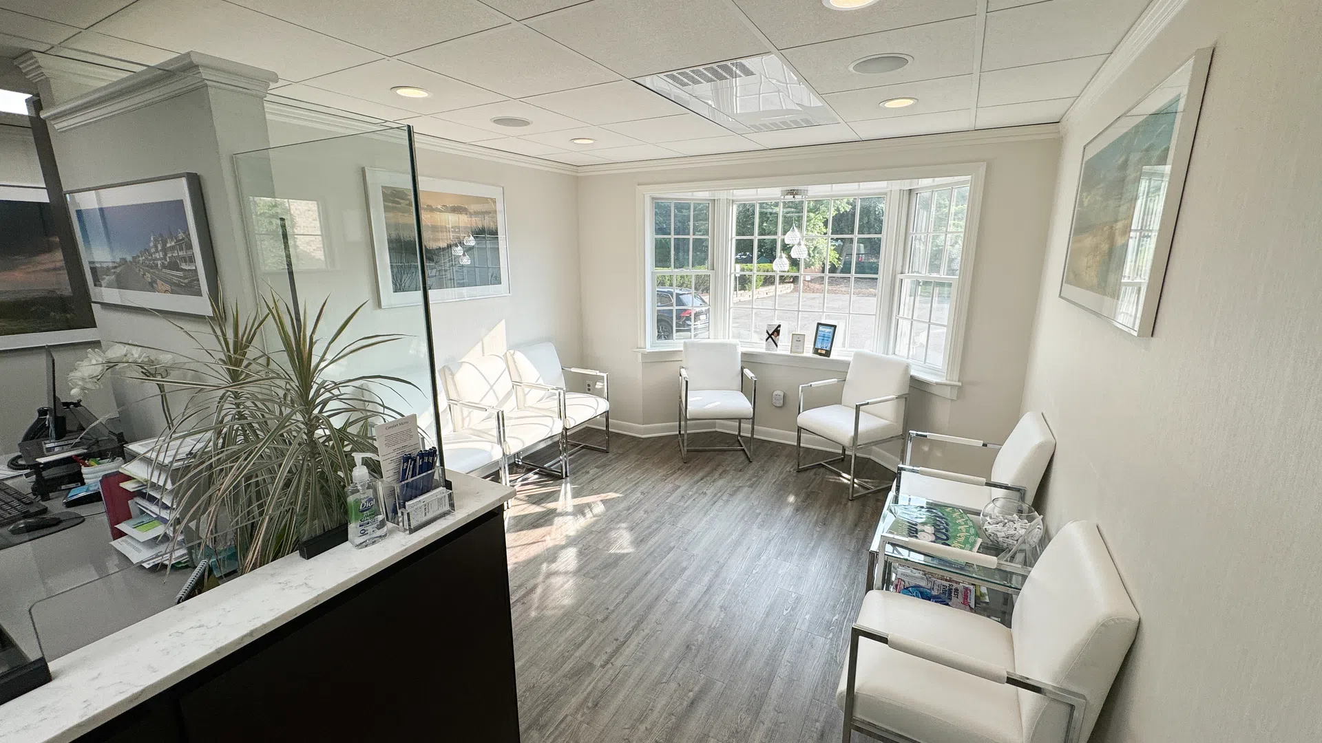 Bright waiting room with white chairs, large windows, wood flooring, and modern decor in a medical office.